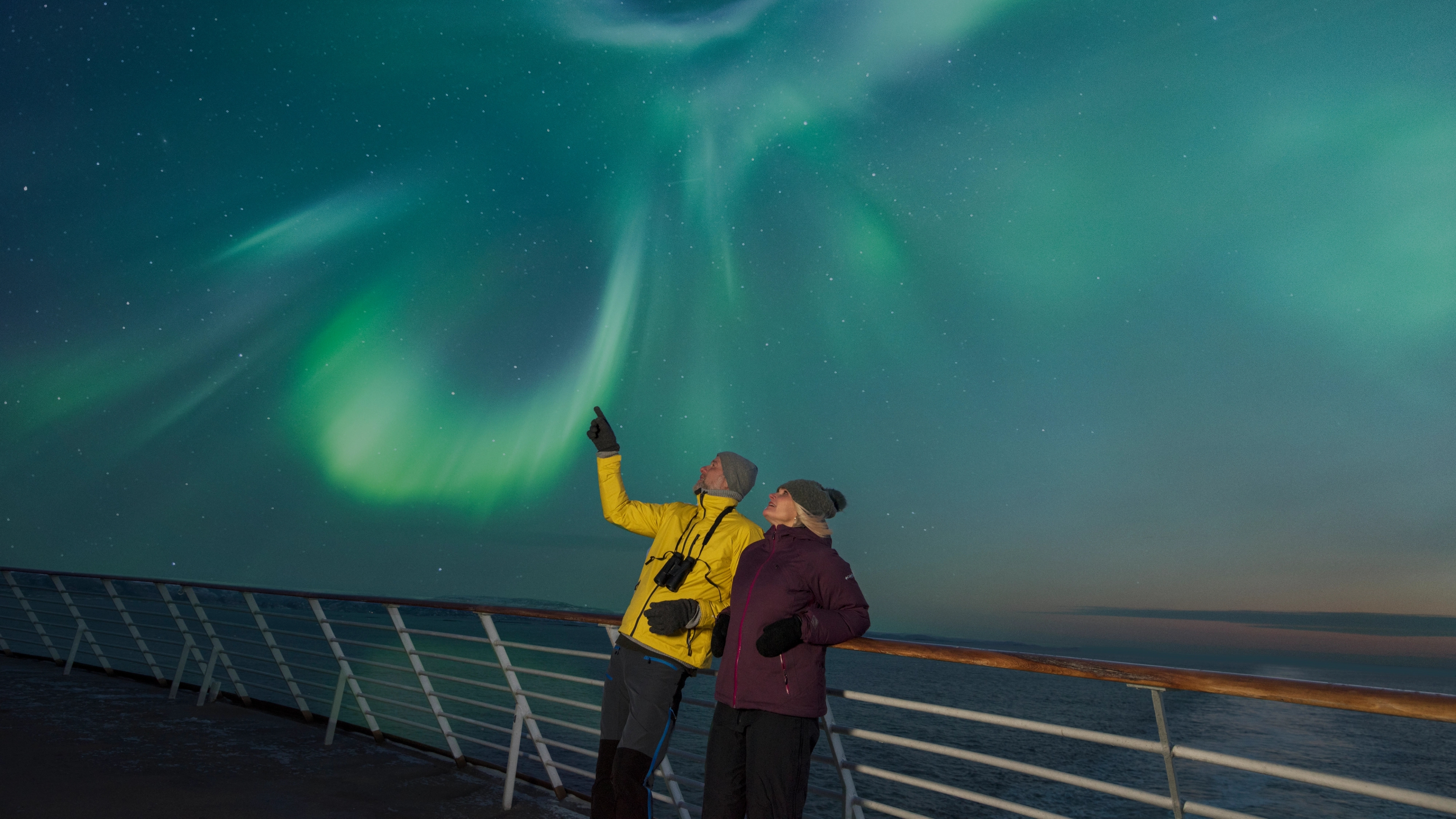 Two people on the deck of a Hurtigruten ship under the norhtern lights in Northern Norway