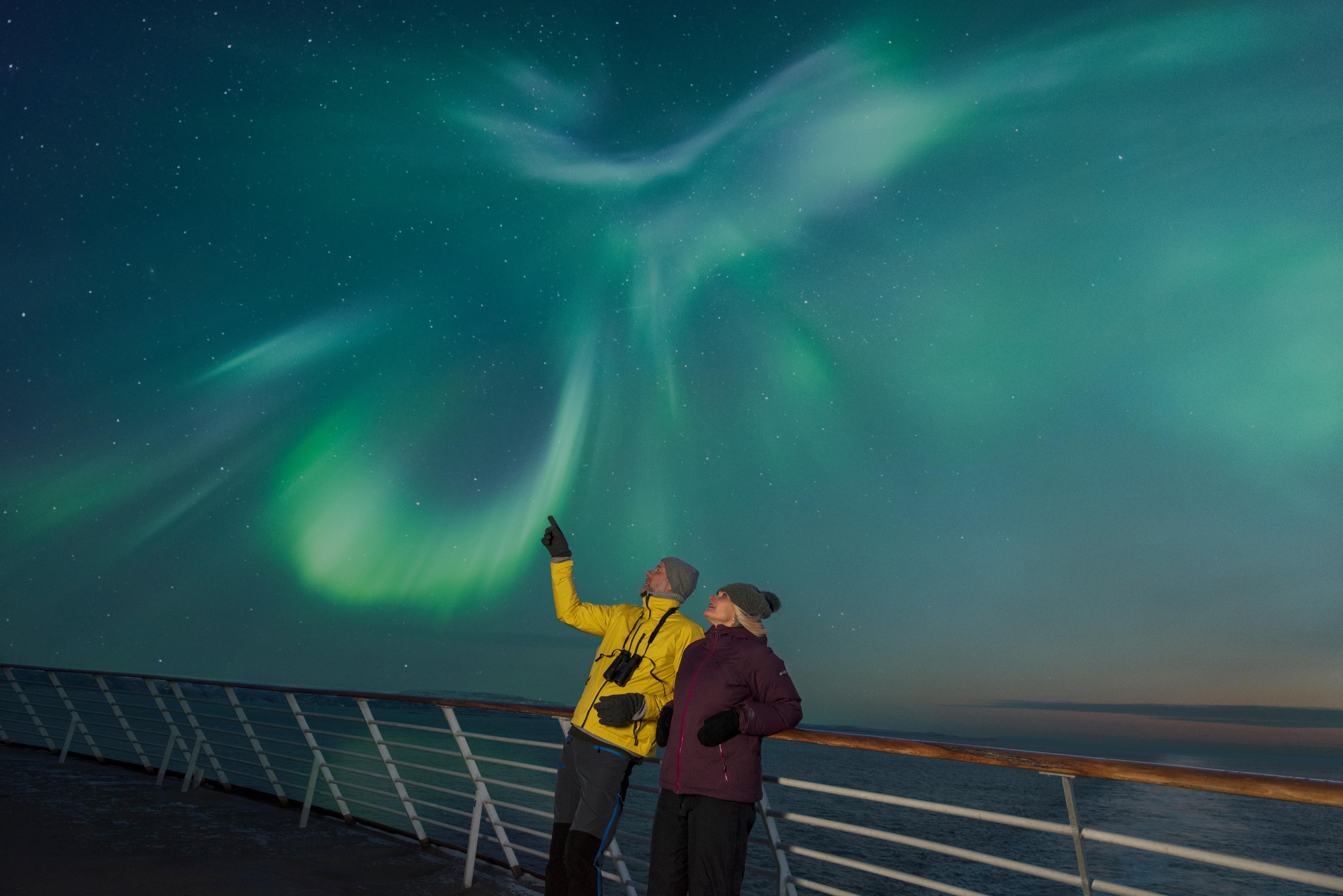 Two people on the deck of a Hurtigruten ship under the norhtern lights in Northern Norway