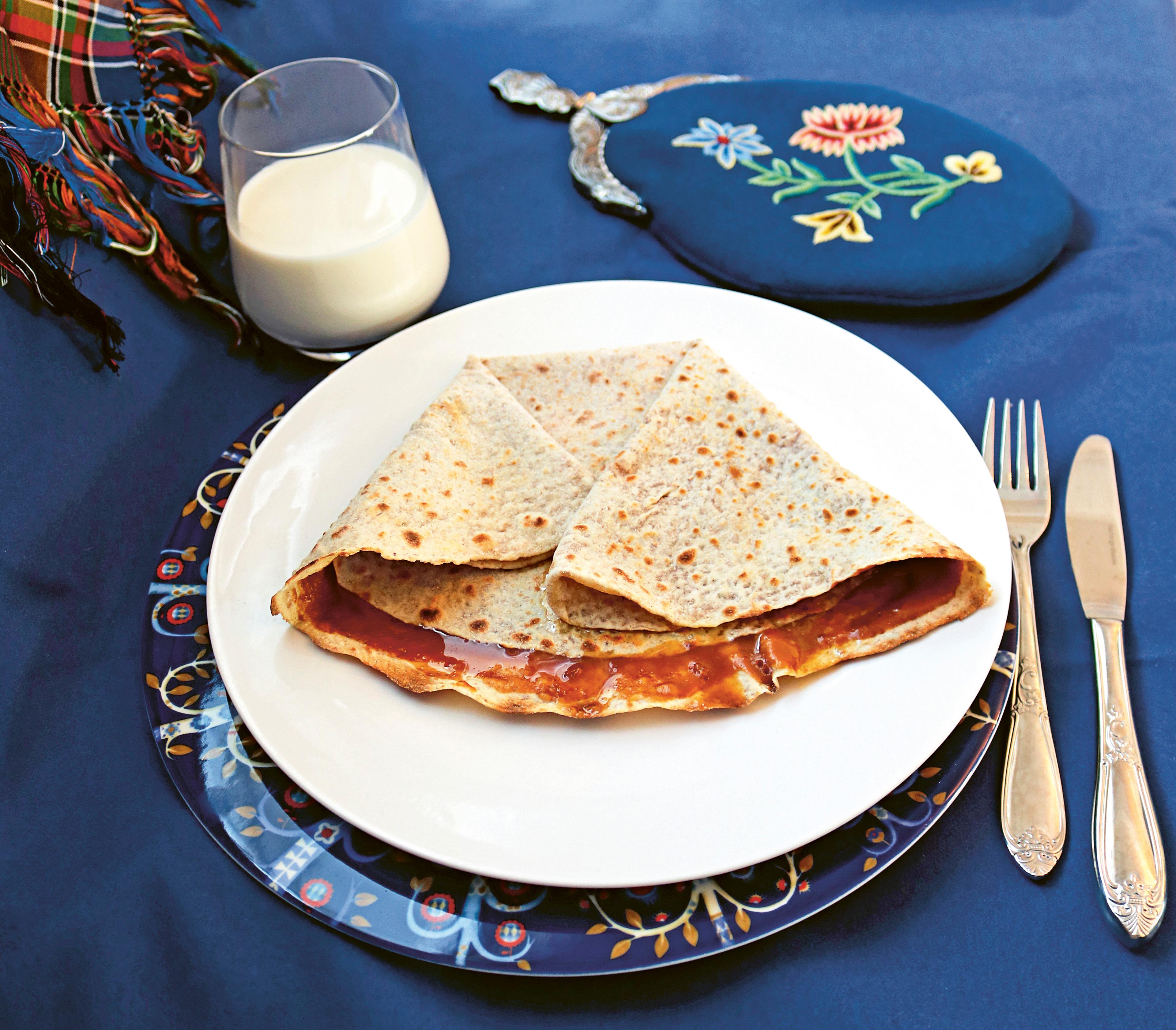 Lefse with a brown cheese spread called "møsbrøm" served on a platter and a glass of milk in Norway