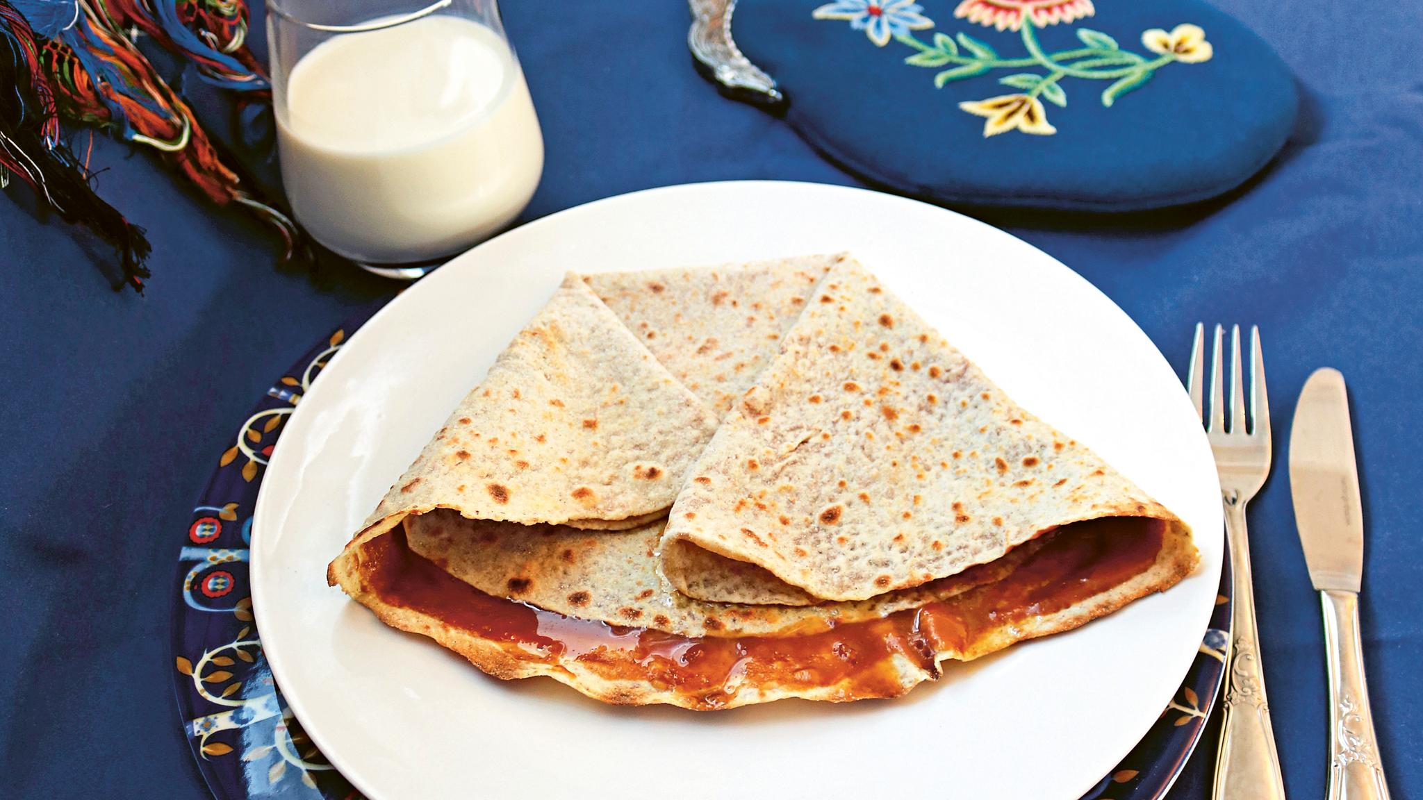 Lefse with a brown cheese spread called "møsbrøm" served on a platter and a glass of milk in Norway