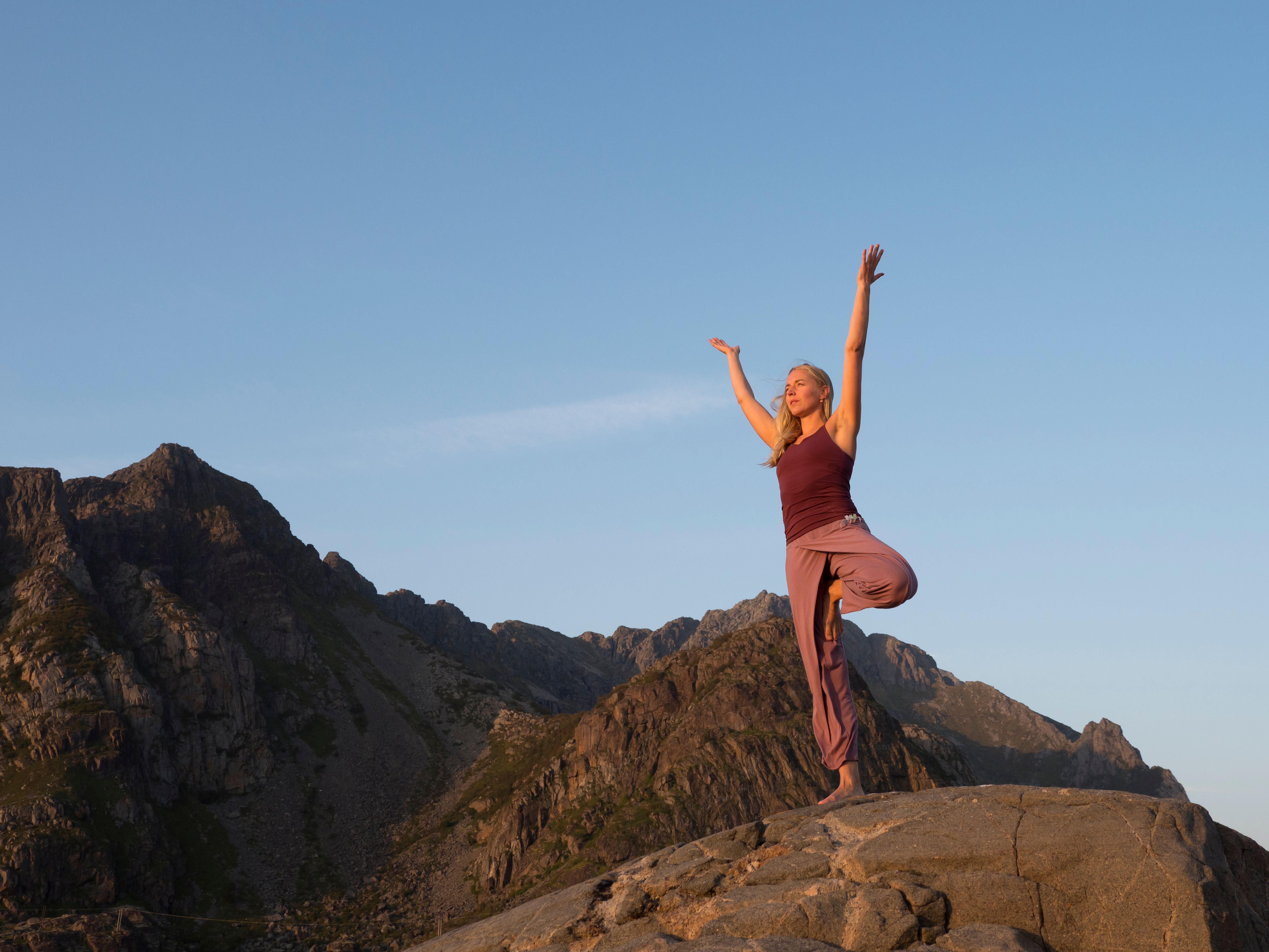 A woman is doing yoga, surrounded by mountains.