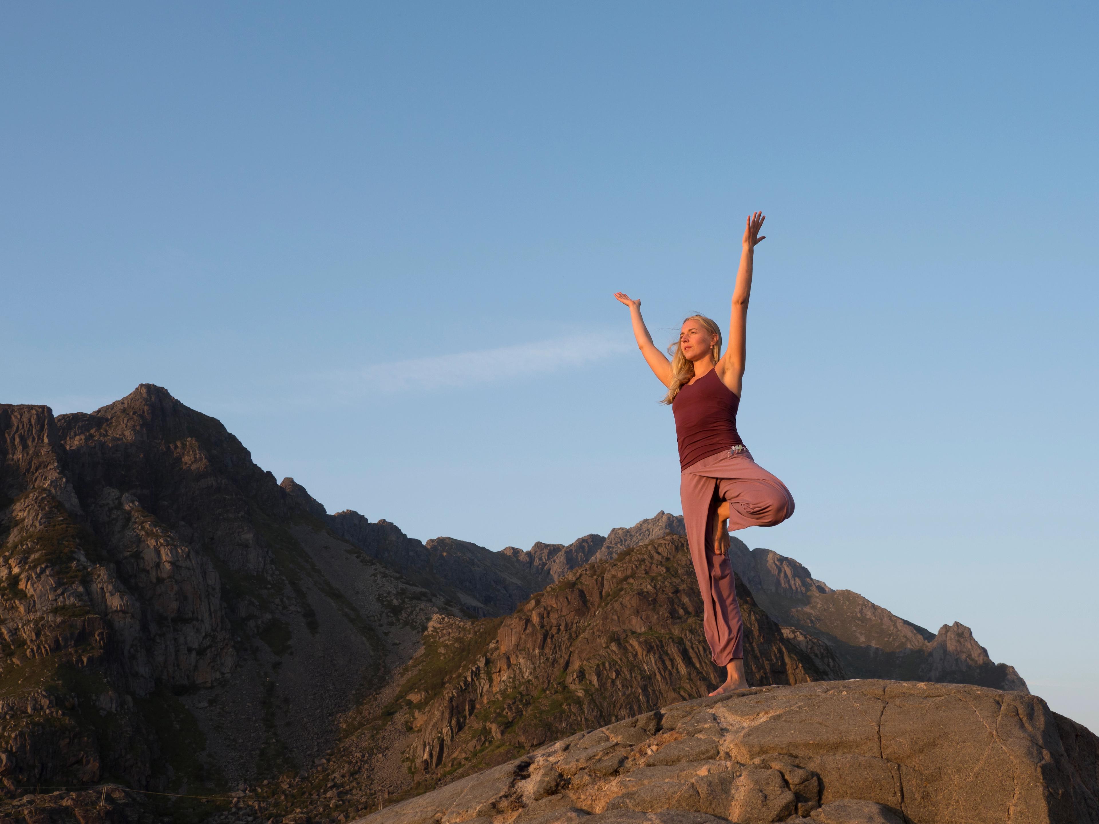 A woman is doing yoga, surrounded by mountains.