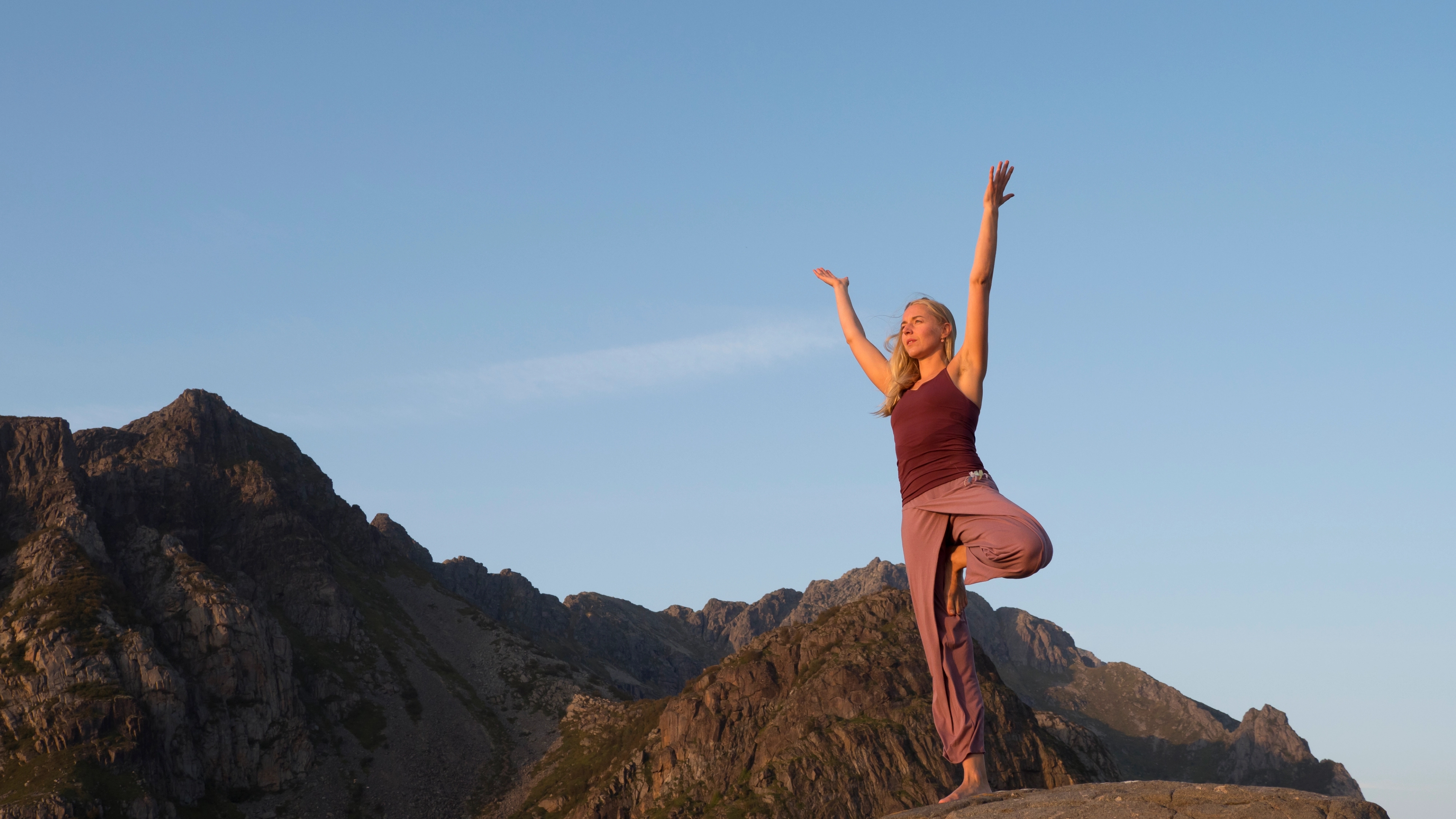 A woman is doing yoga, surrounded by mountains.