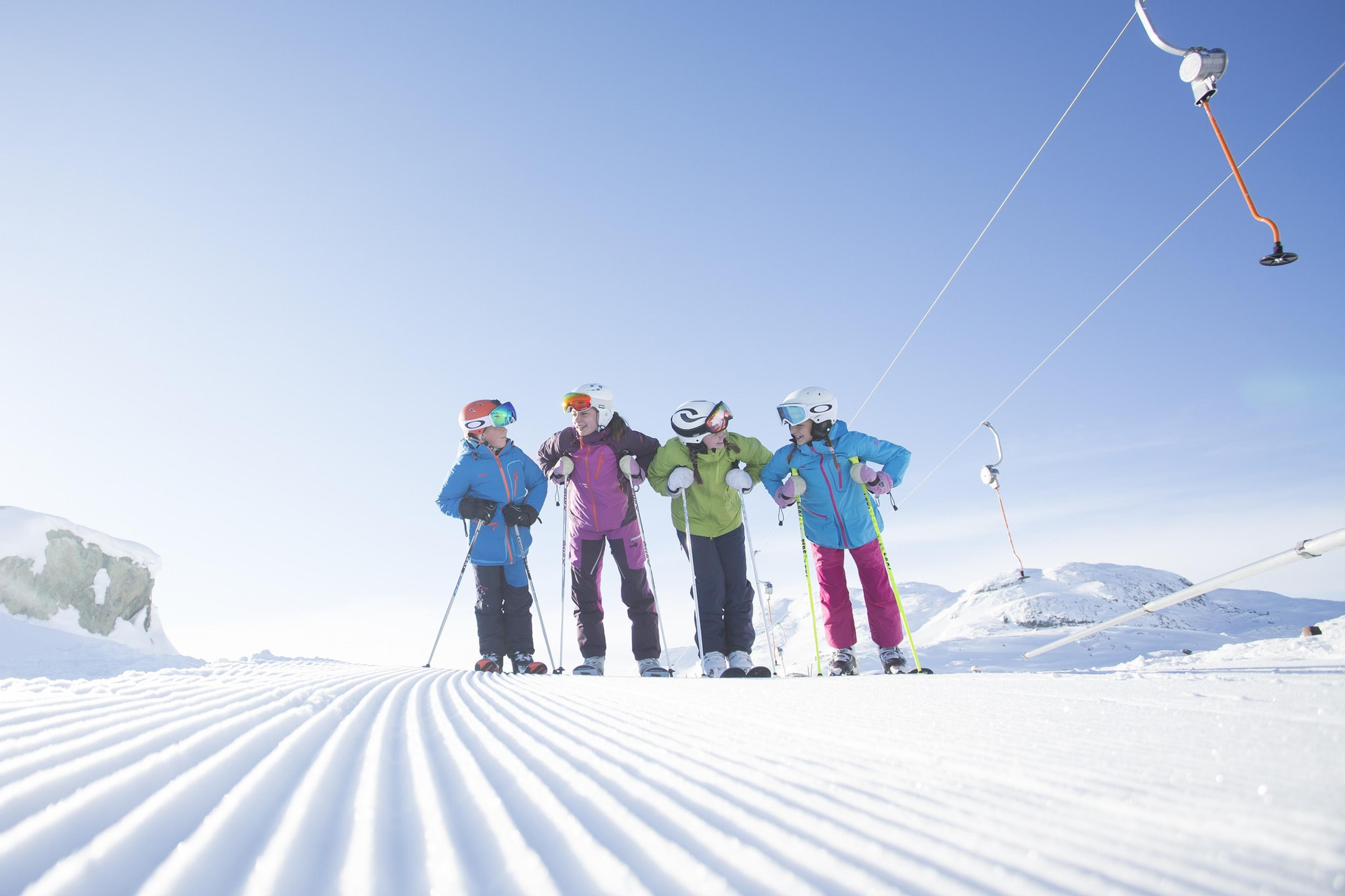 Four kids with skiers stand on a freshly groomed slope next to a button lift in Hemsedal, Eastern Norway