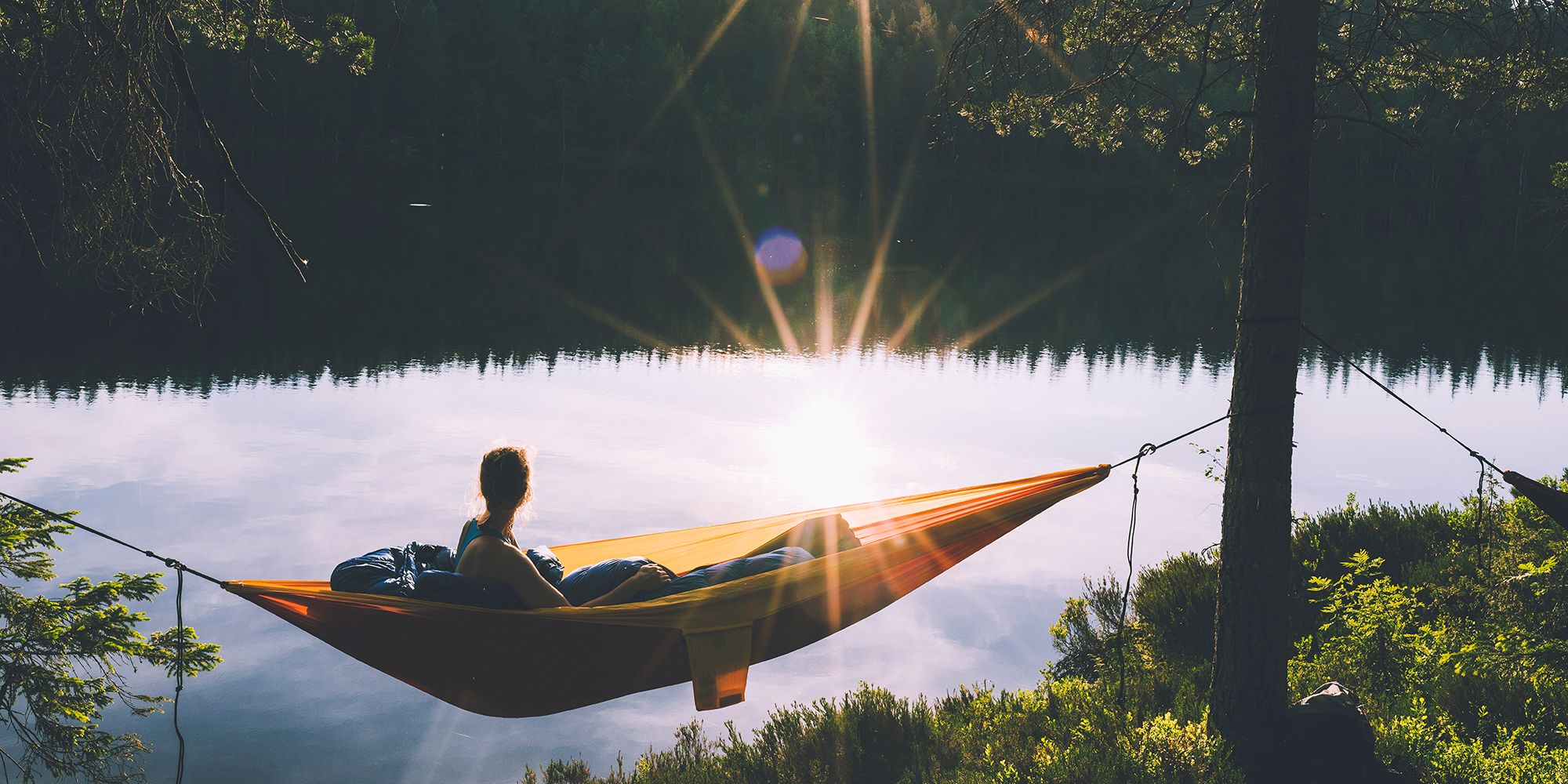 En dame ligger og slapper av i en hengekøye mens sola går ned i Nordmarka i Oslo på Østlandet
