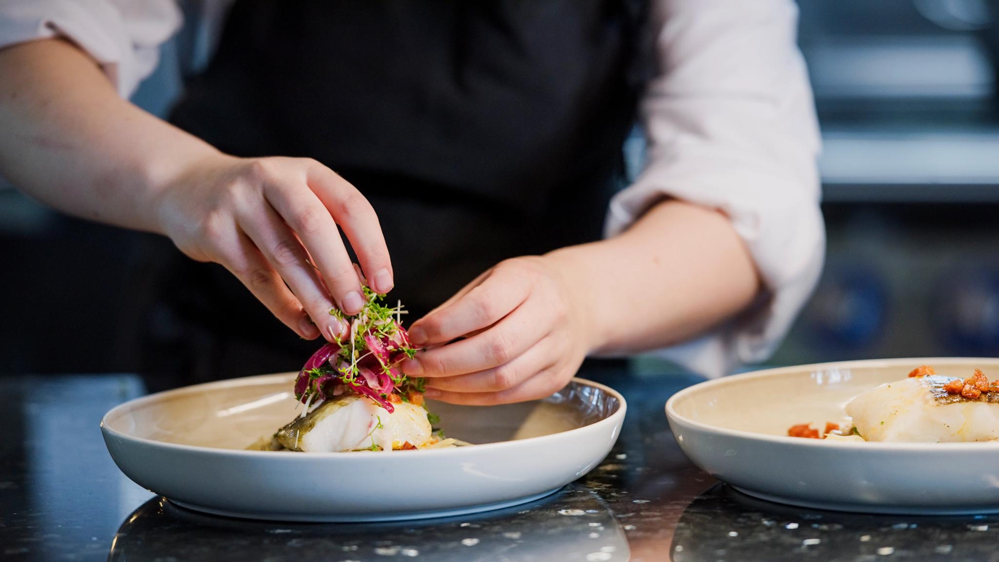 A person preparing a fancy dish at the Norway’s coastal kitchen at a Hurtigruten ship