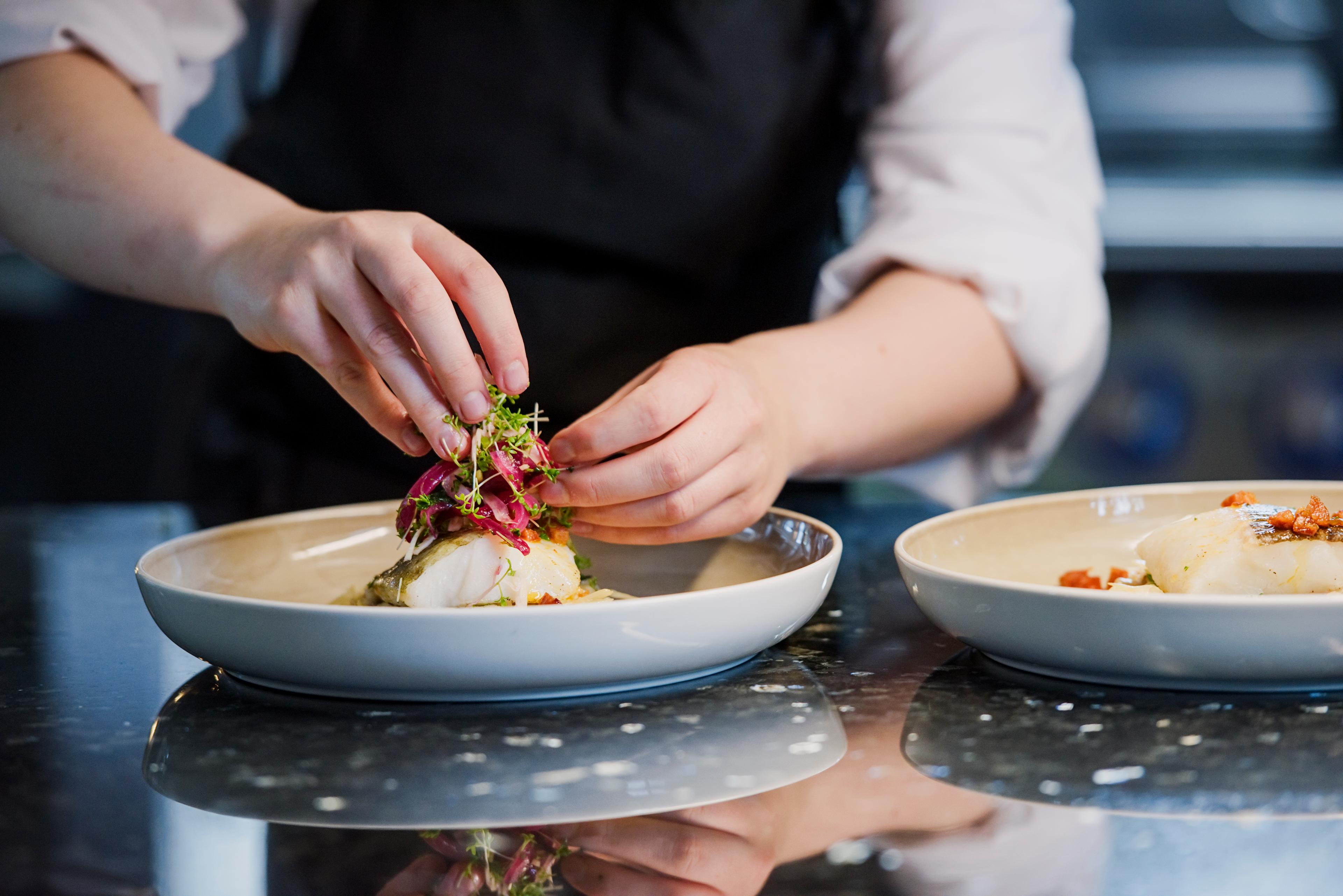 A person preparing a fancy dish at the Norway’s coastal kitchen at a Hurtigruten ship
