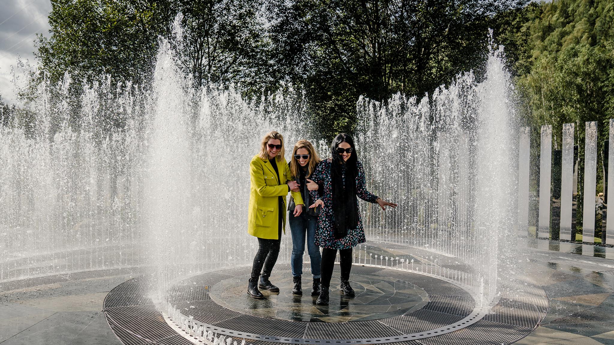 Four laughing women standing in the fountain surrounded by mirrors at Kistefos Museum in Hadeland