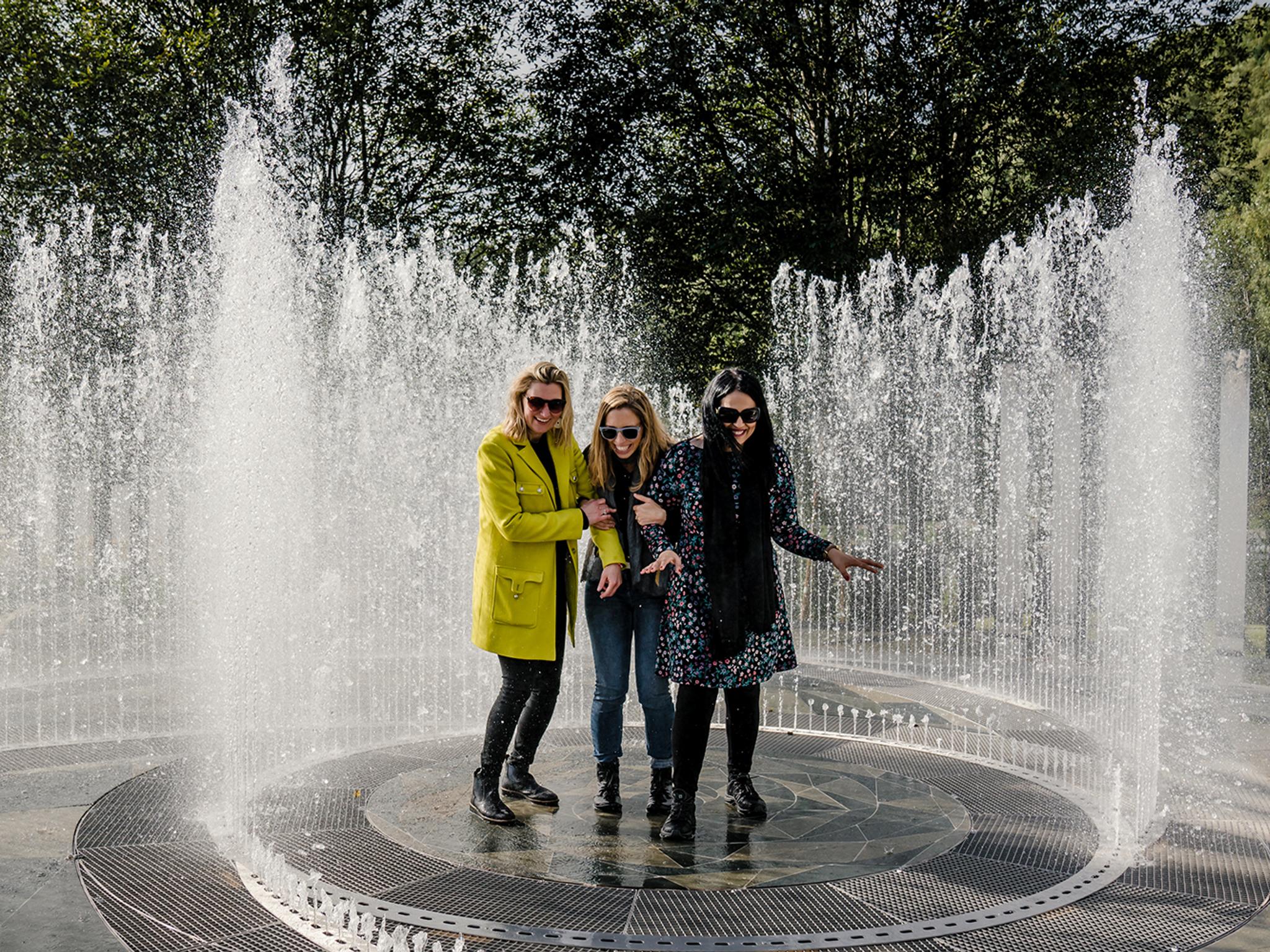 Four laughing women standing in the fountain surrounded by mirrors at Kistefos Museum in Hadeland