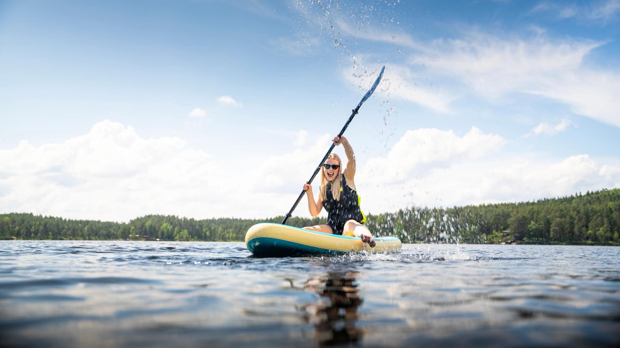 A girl rowing whilst sat on a paddle board