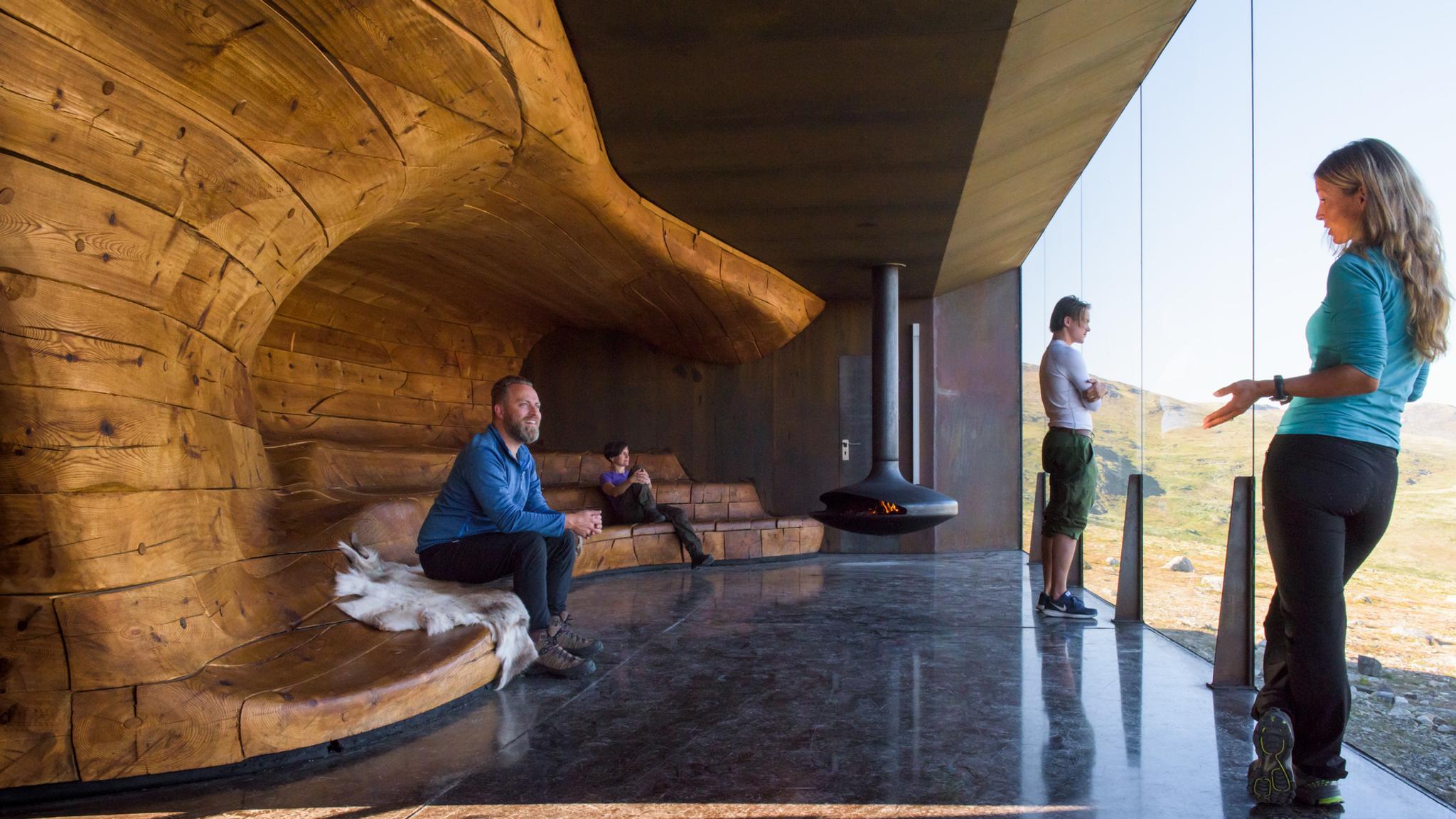 People enjoying the view from a wooden bench in a room with giant windows.
