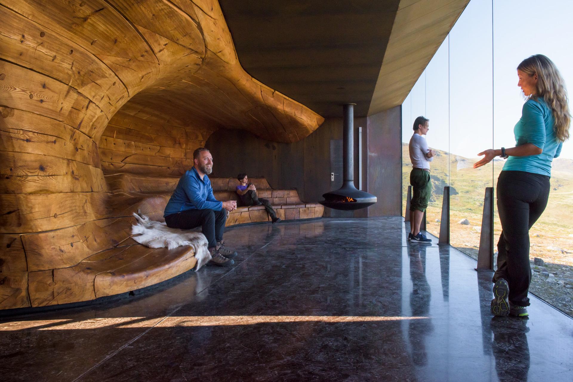People enjoying the view from a wooden bench in a room with giant windows.