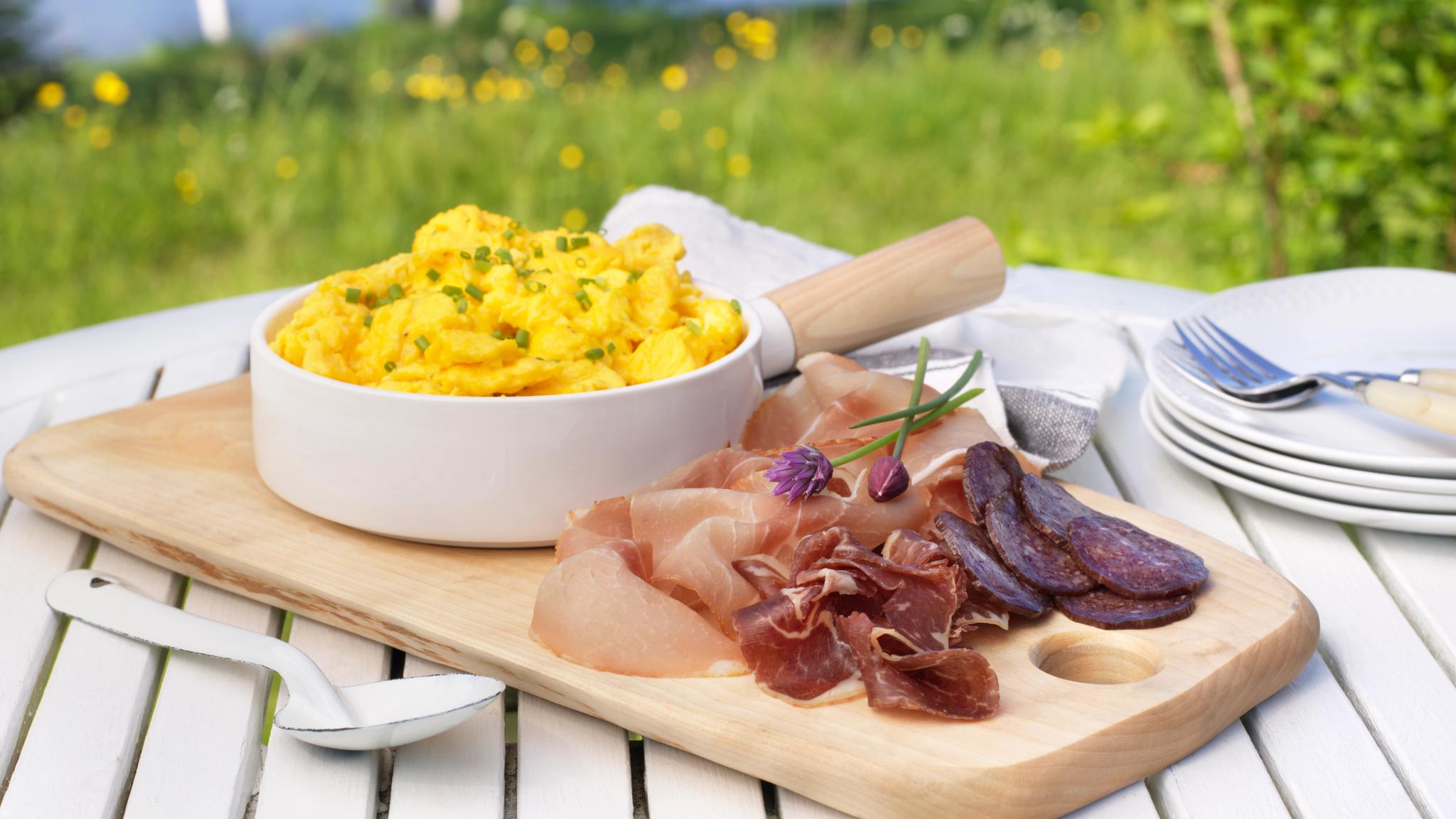 A serving of cured meat and a bowl of scrambled eggs in the garden.