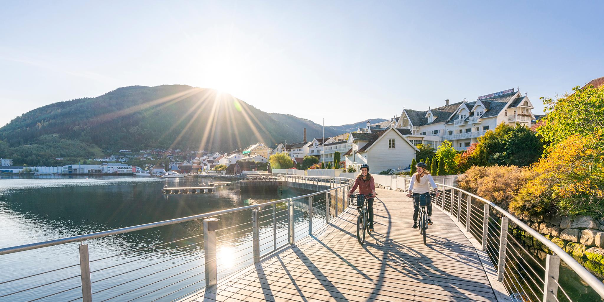 Plan your trip to the Sognefjord area: Two women are biking along the Fjordstien path in Sogndal by the Sognefjord in Fjord Norway