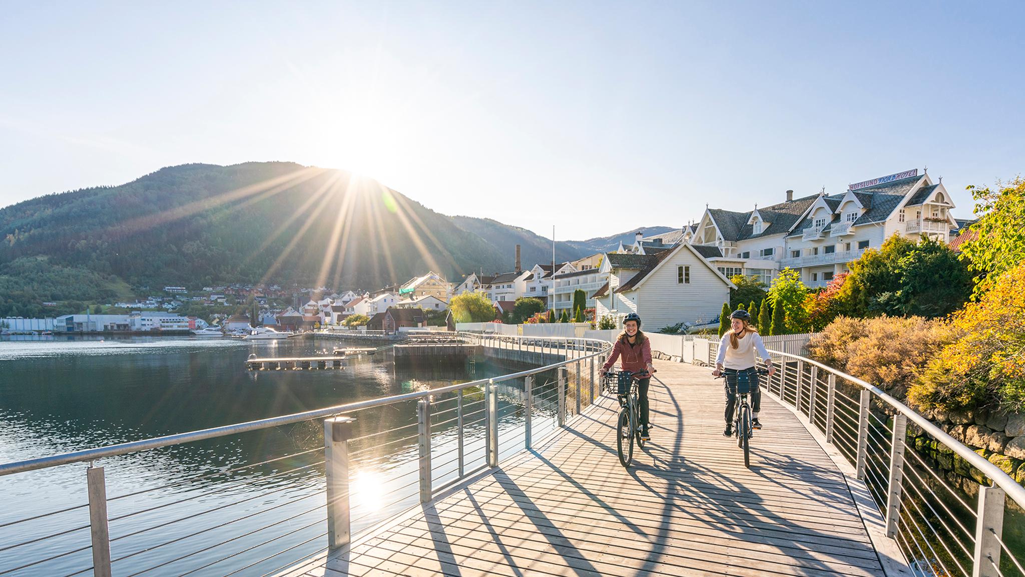 Plan your trip to the Sognefjord area: Two women are biking along the Fjordstien path in Sogndal by the Sognefjord in Fjord Norway