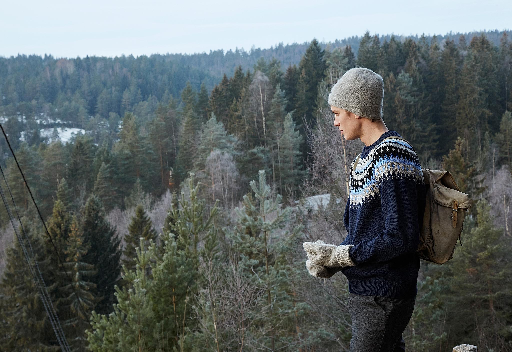 A guy in a woollen sweater looking over the treetops of a forest