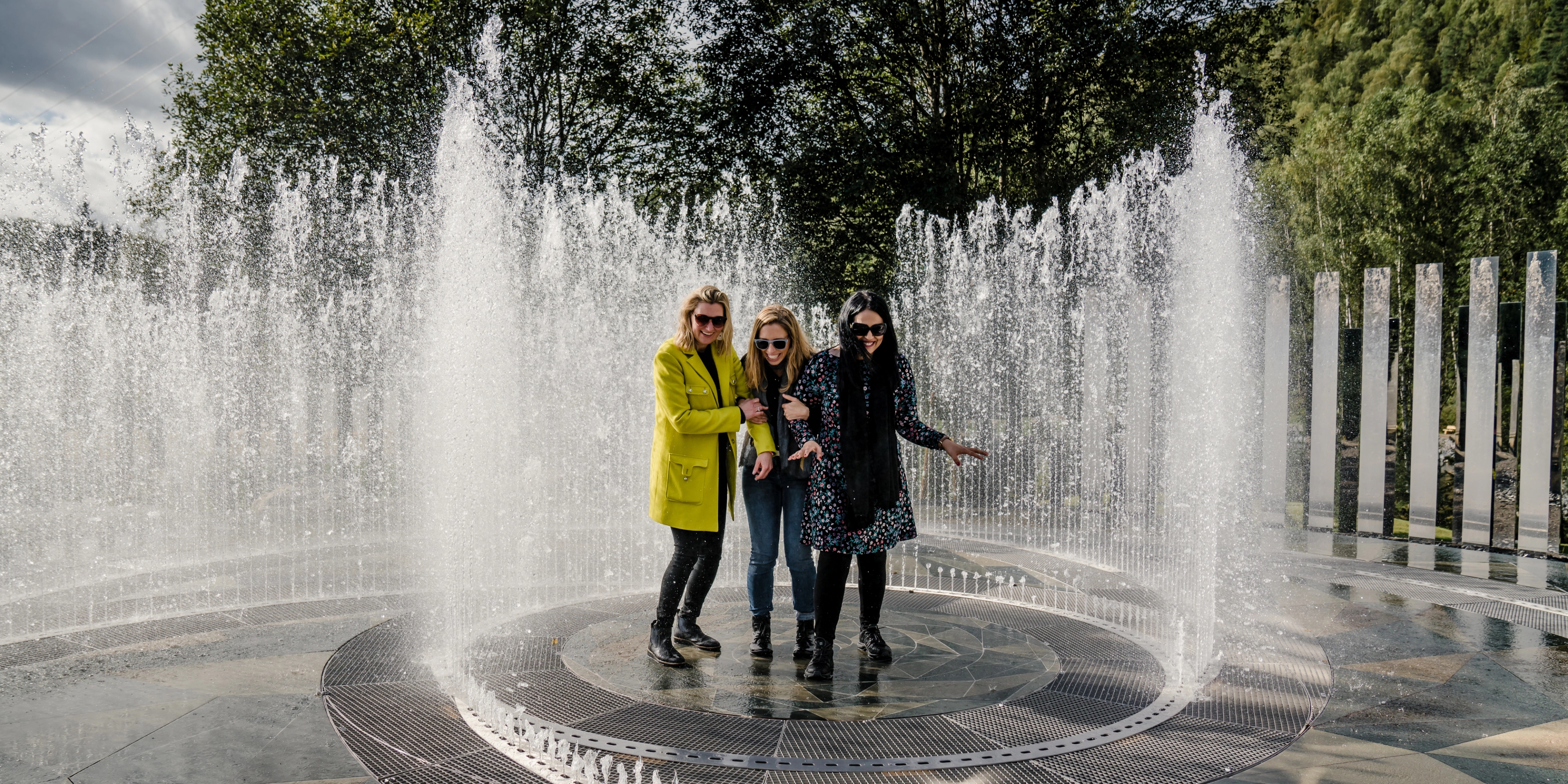 Fire glade kvinner står i fontenen omringet av speil på Kistefos-Museet på Hadeland