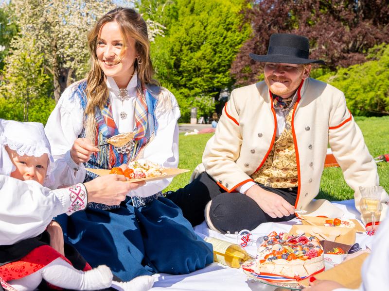 Folk nyter 17. mai buffet i parken iført bunad på nasjonaldagen, 17. mai