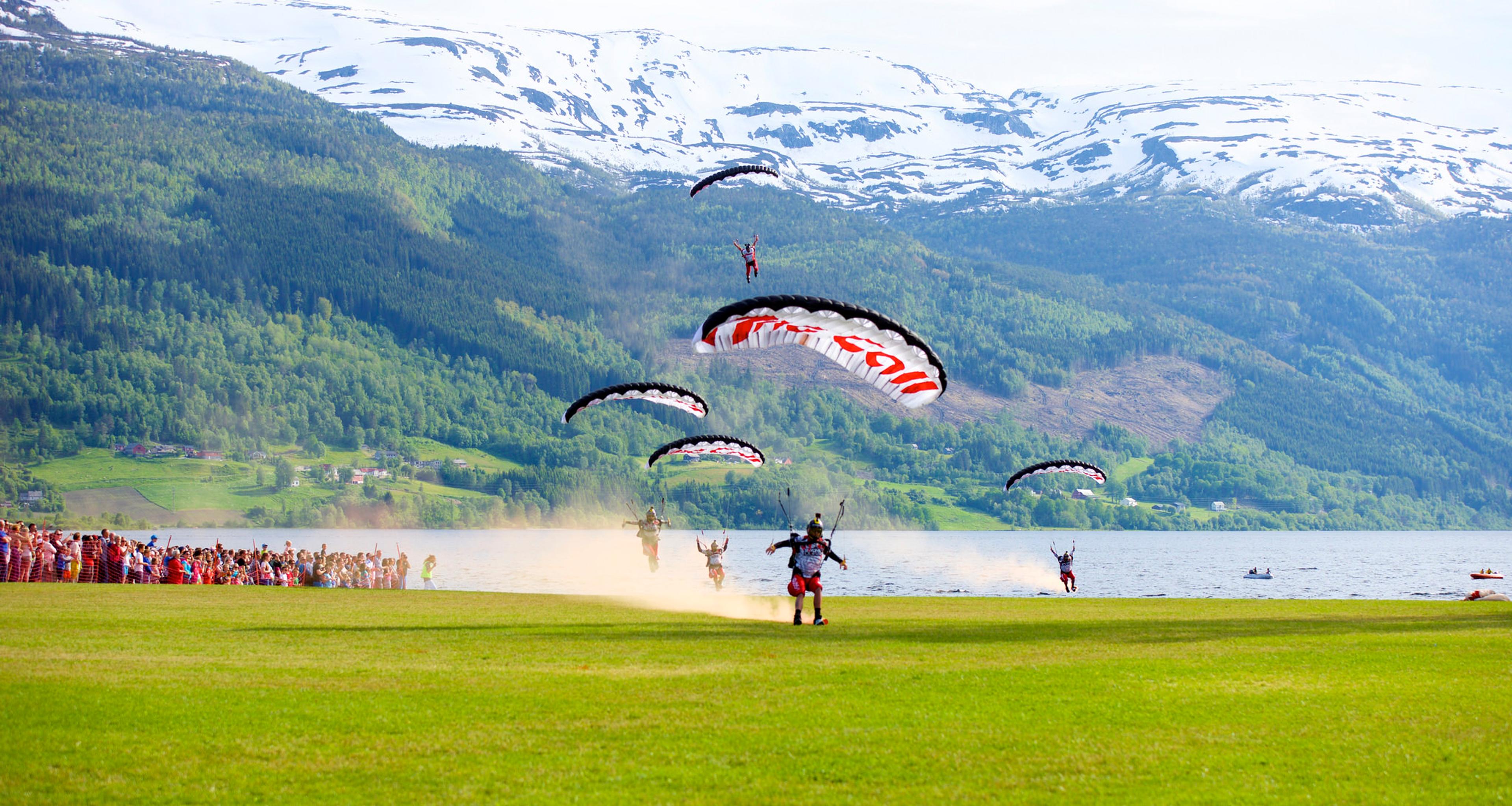 A group of paragliders landing on a green field in Voss in Fjord Norway during the Ekstremsportveko extreme sport festival