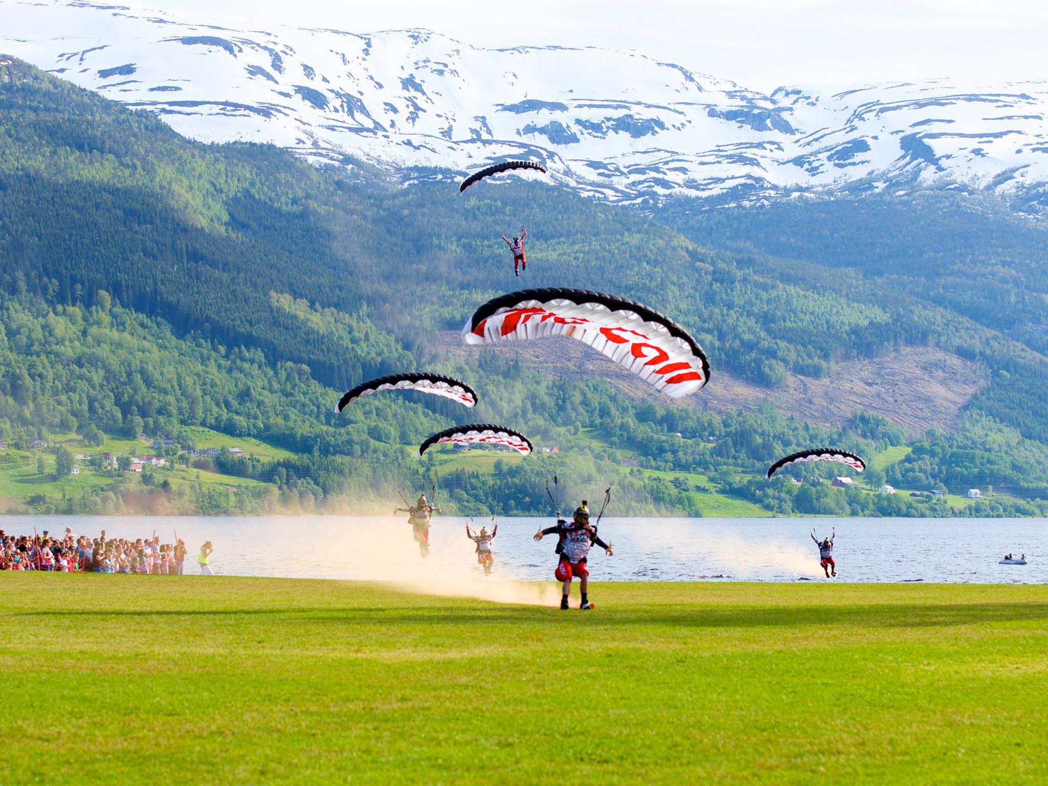A group of paragliders landing on a green field in Voss in Fjord Norway during the Ekstremsportveko extreme sport festival