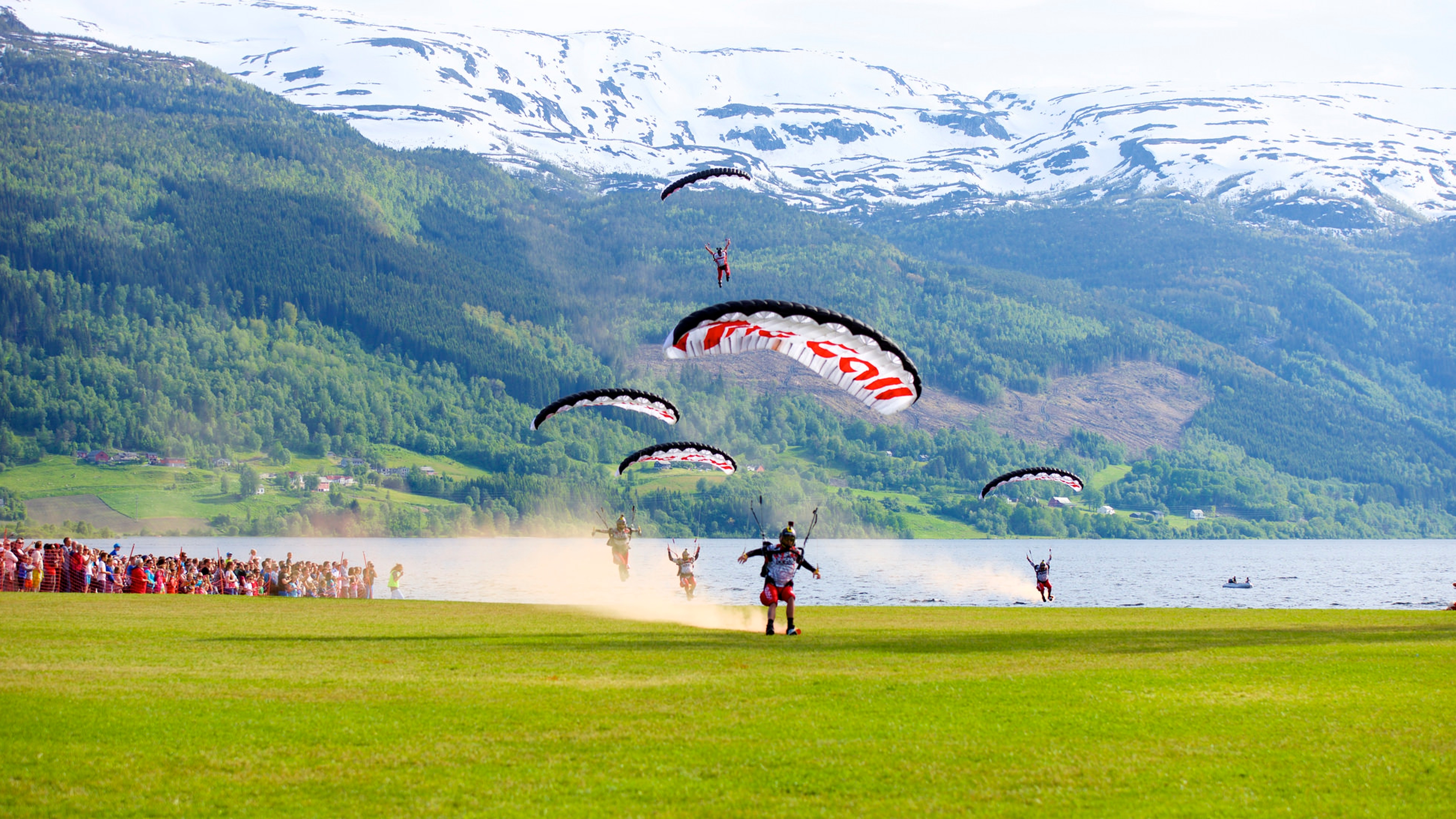 A group of paragliders landing on a green field in Voss in Fjord Norway during the Ekstremsportveko extreme sport festival