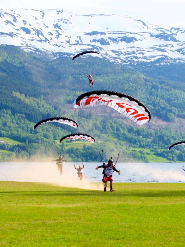 A group of paragliders landing on a green field in Voss in Fjord Norway during the Ekstremsportveko extreme sport festival