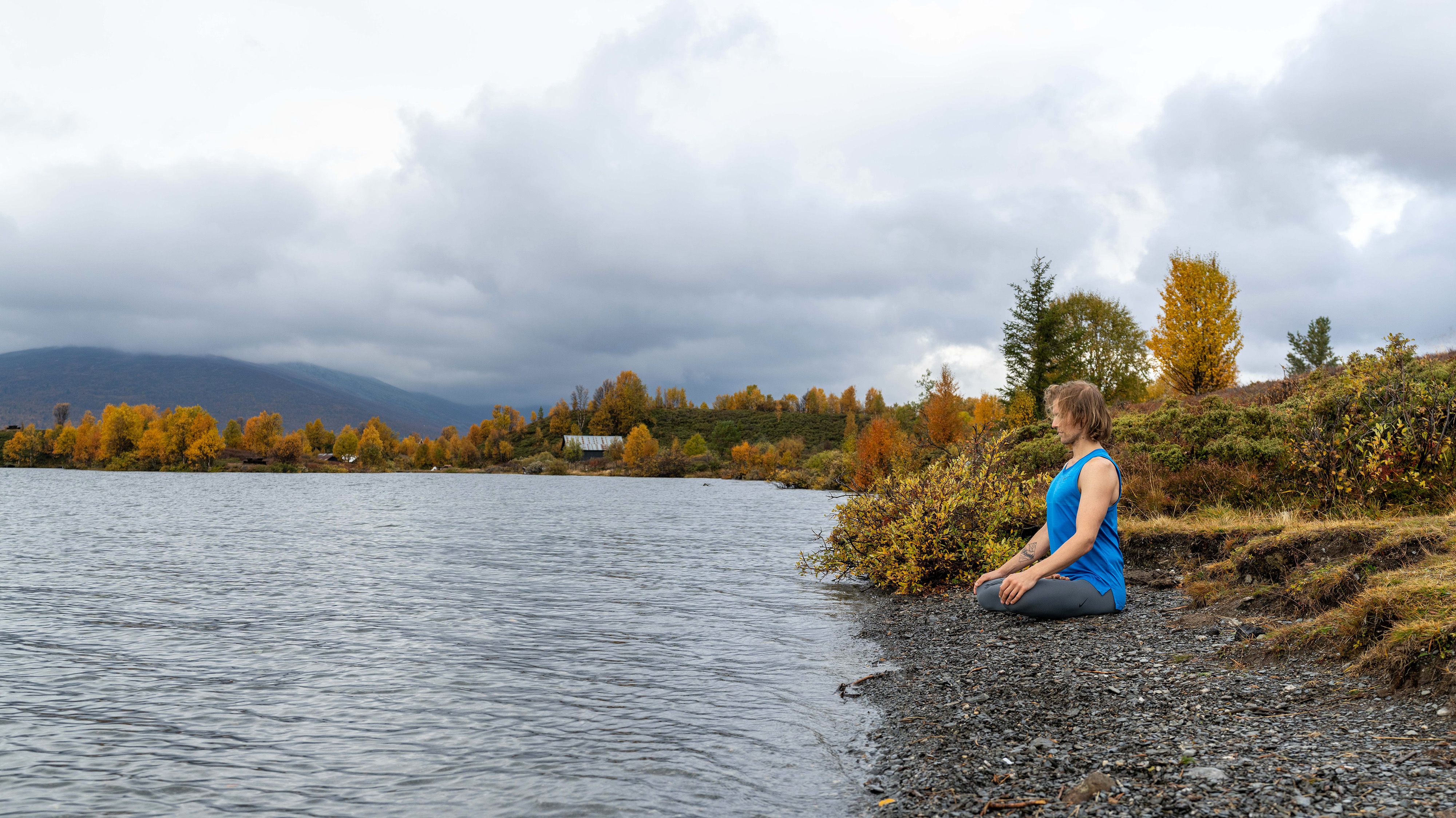 A man meditating in lotus position by the water at Nøsen yoga and mountain hotel in Eastern Norway