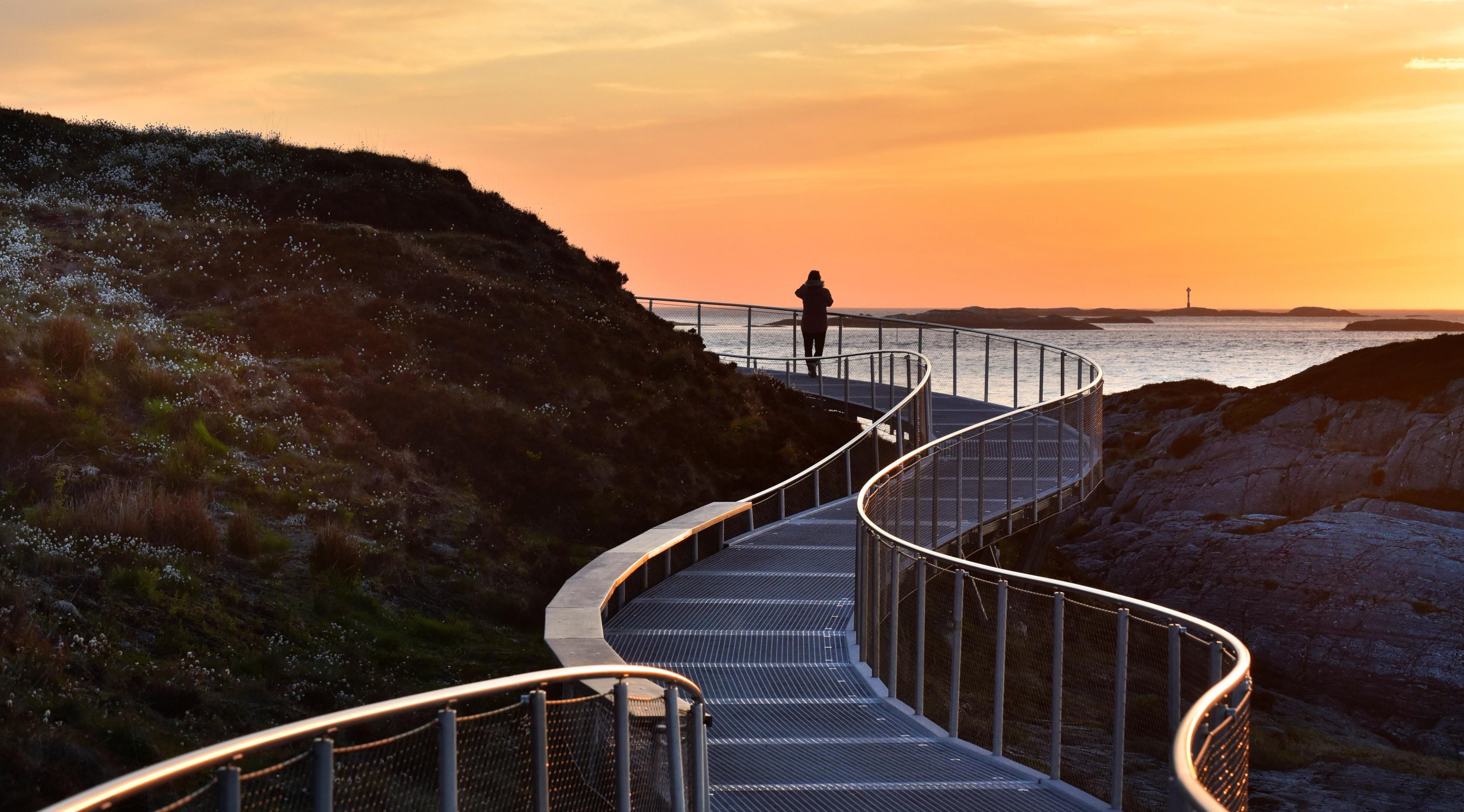 A person standing on The Atlantic Road by Eldhusøya at sunset. Fjord Norway.