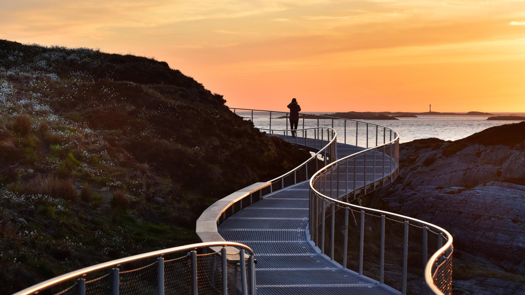A person standing on The Atlantic Road by Eldhusøya at sunset. Fjord Norway.