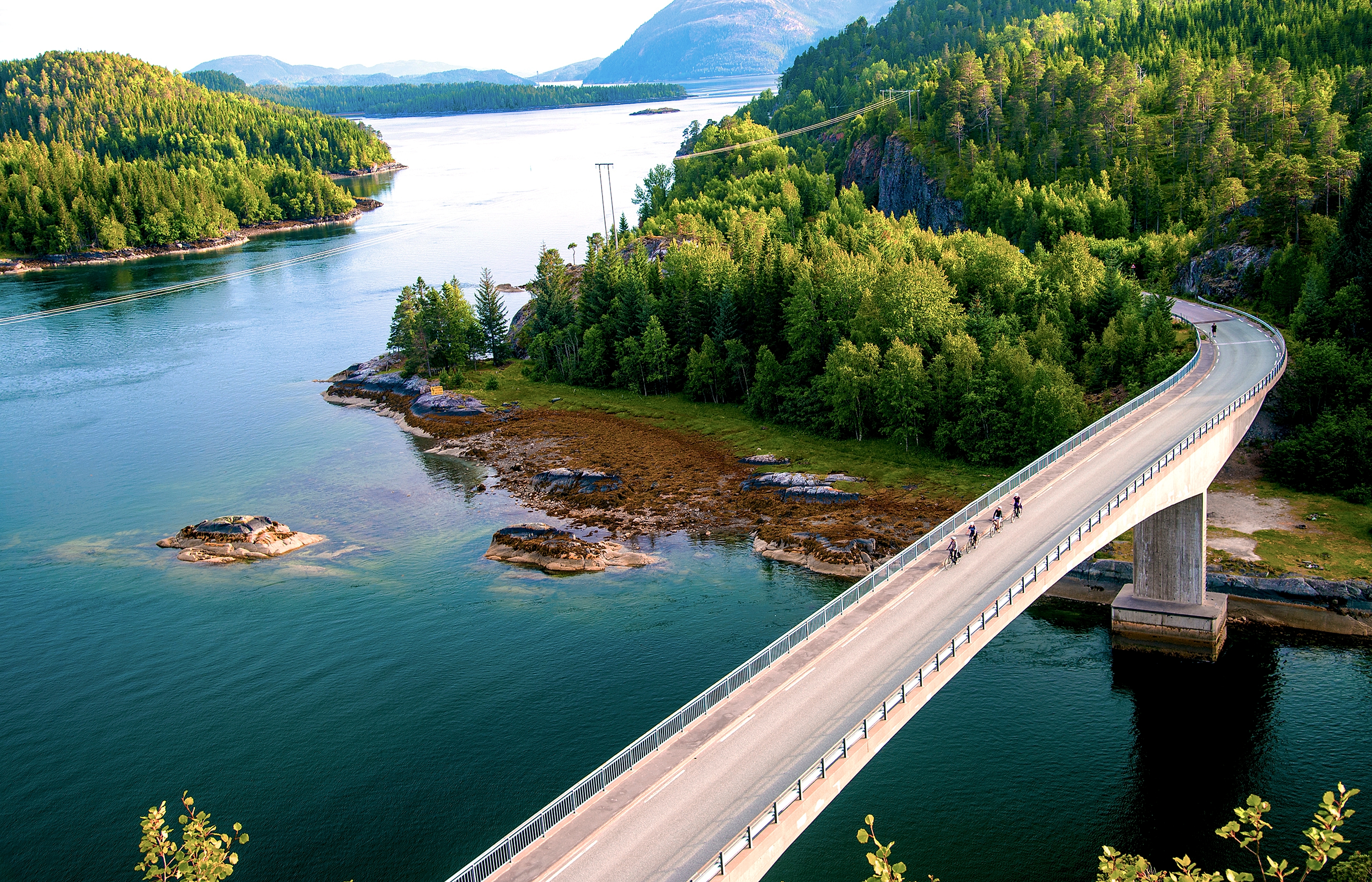 People cycling across a bridge at the Namdalskysten coast in Trøndelag on a sunny summer day