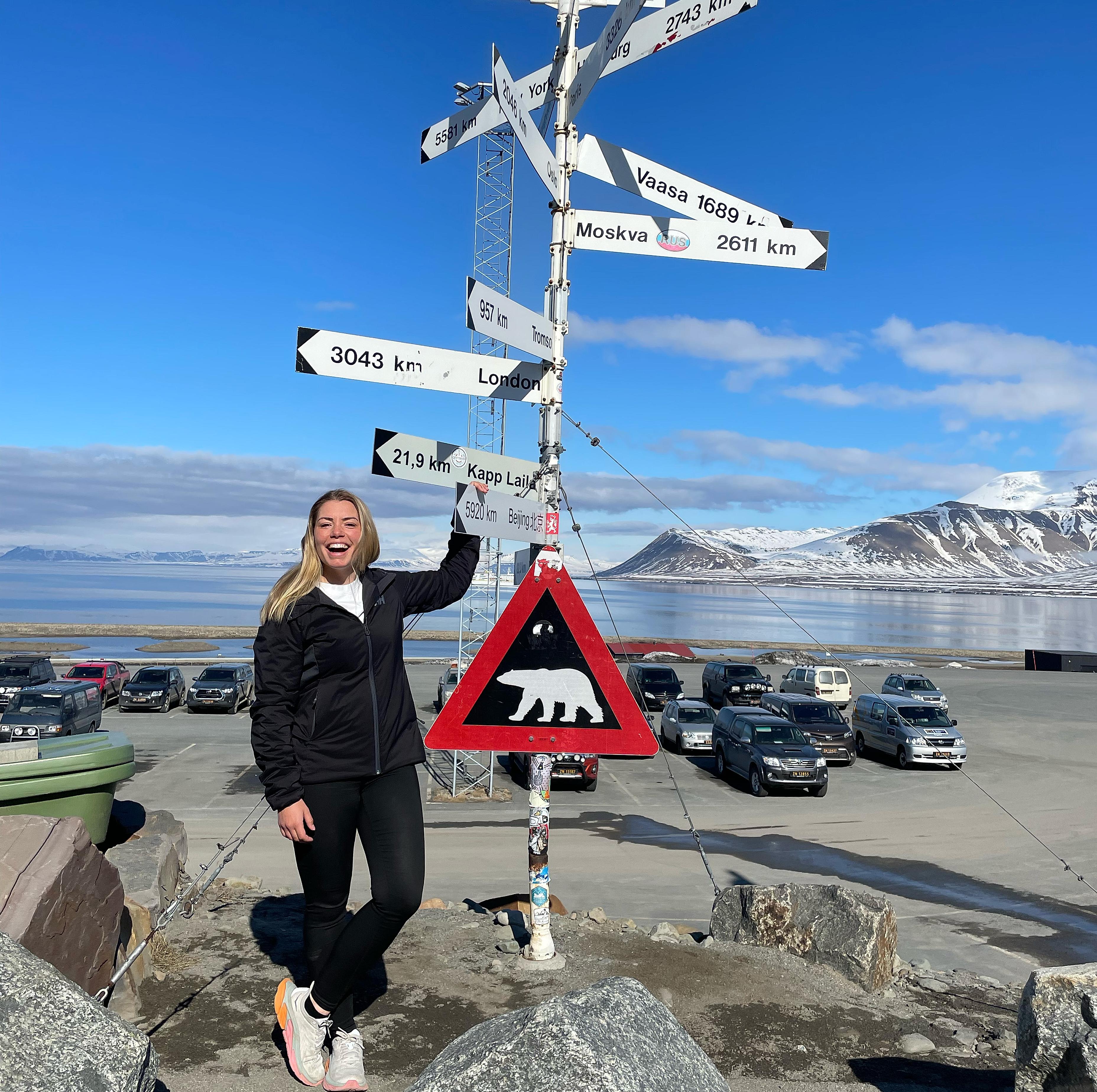 A woman laughing while posing besides the famous polar bear traffic sign at Svalbard