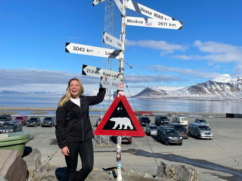 A woman laughing while posing besides the famous polar bear traffic sign at Svalbard