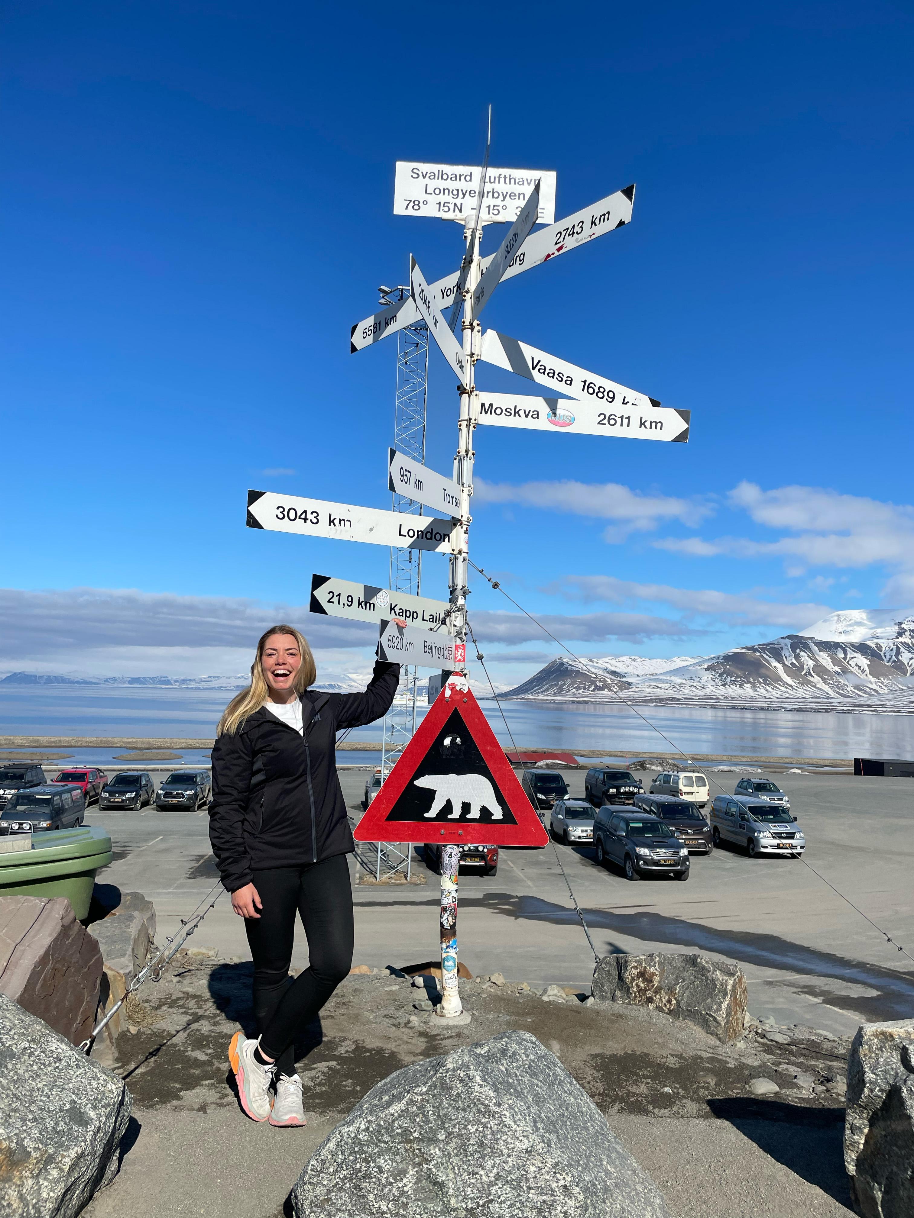 A woman laughing while posing besides the famous polar bear traffic sign at Svalbard