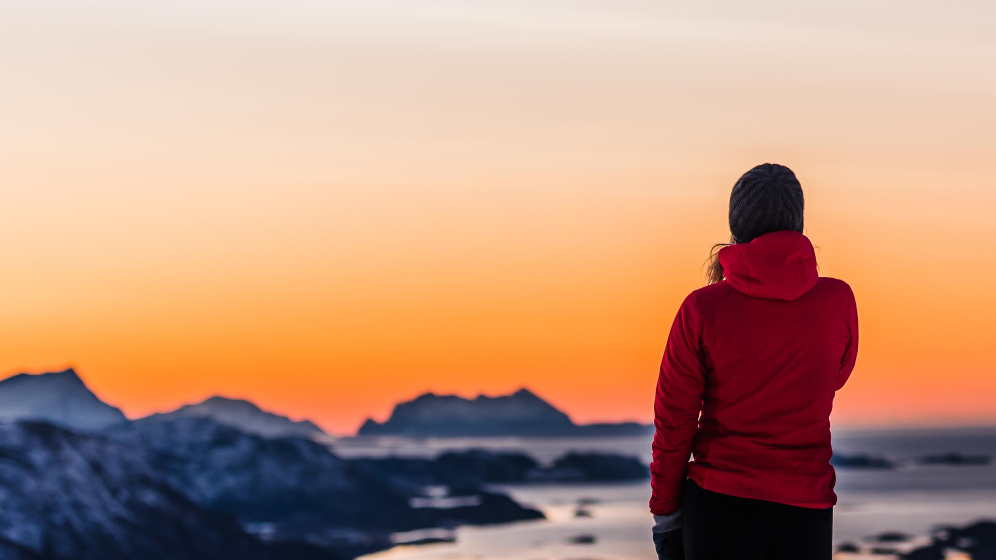 A person looking at the view from a mountain with orange sky.