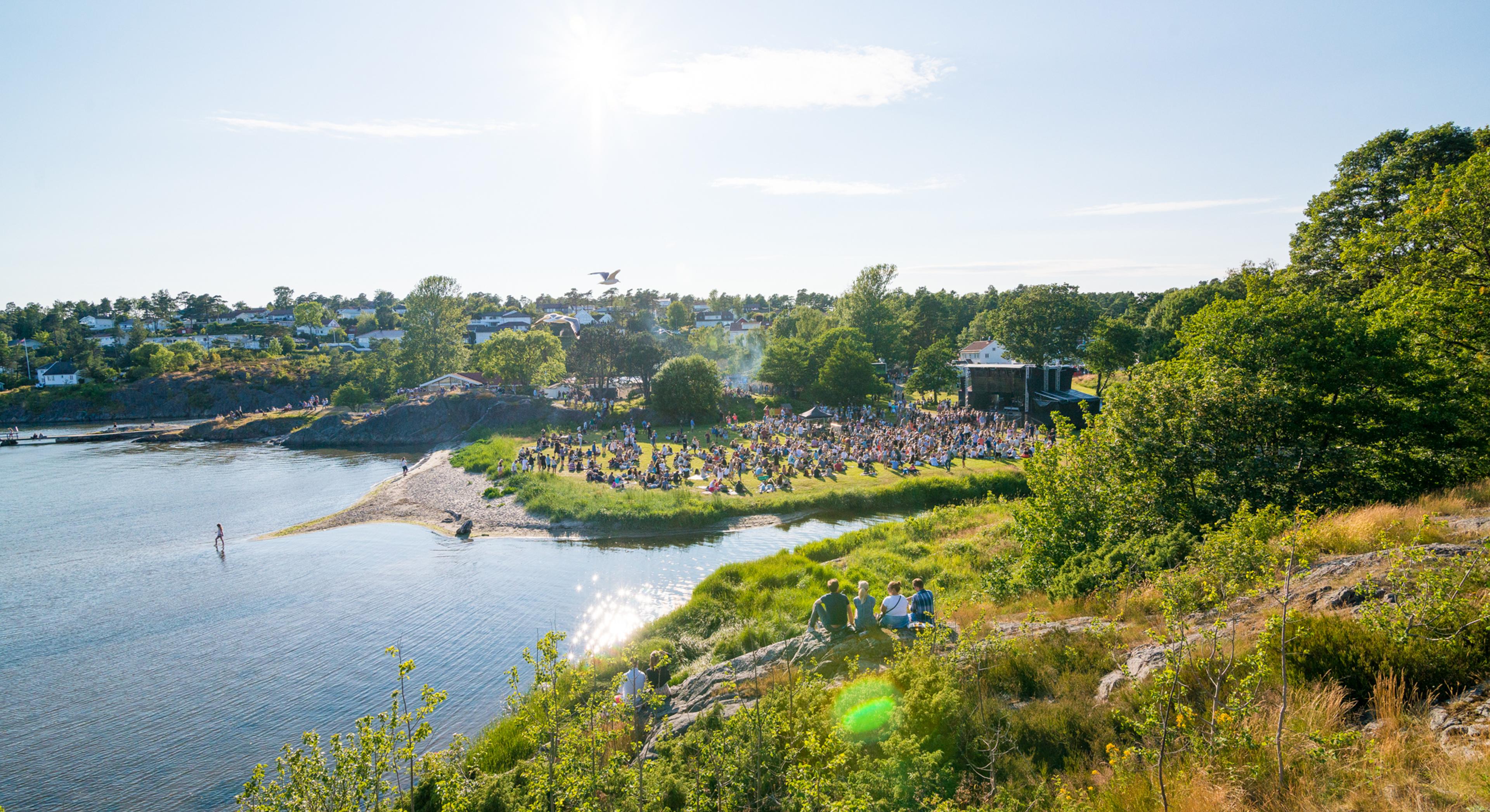 People sitting on the grass by the sea during Skral Festival in Grimstad in Southern Norway