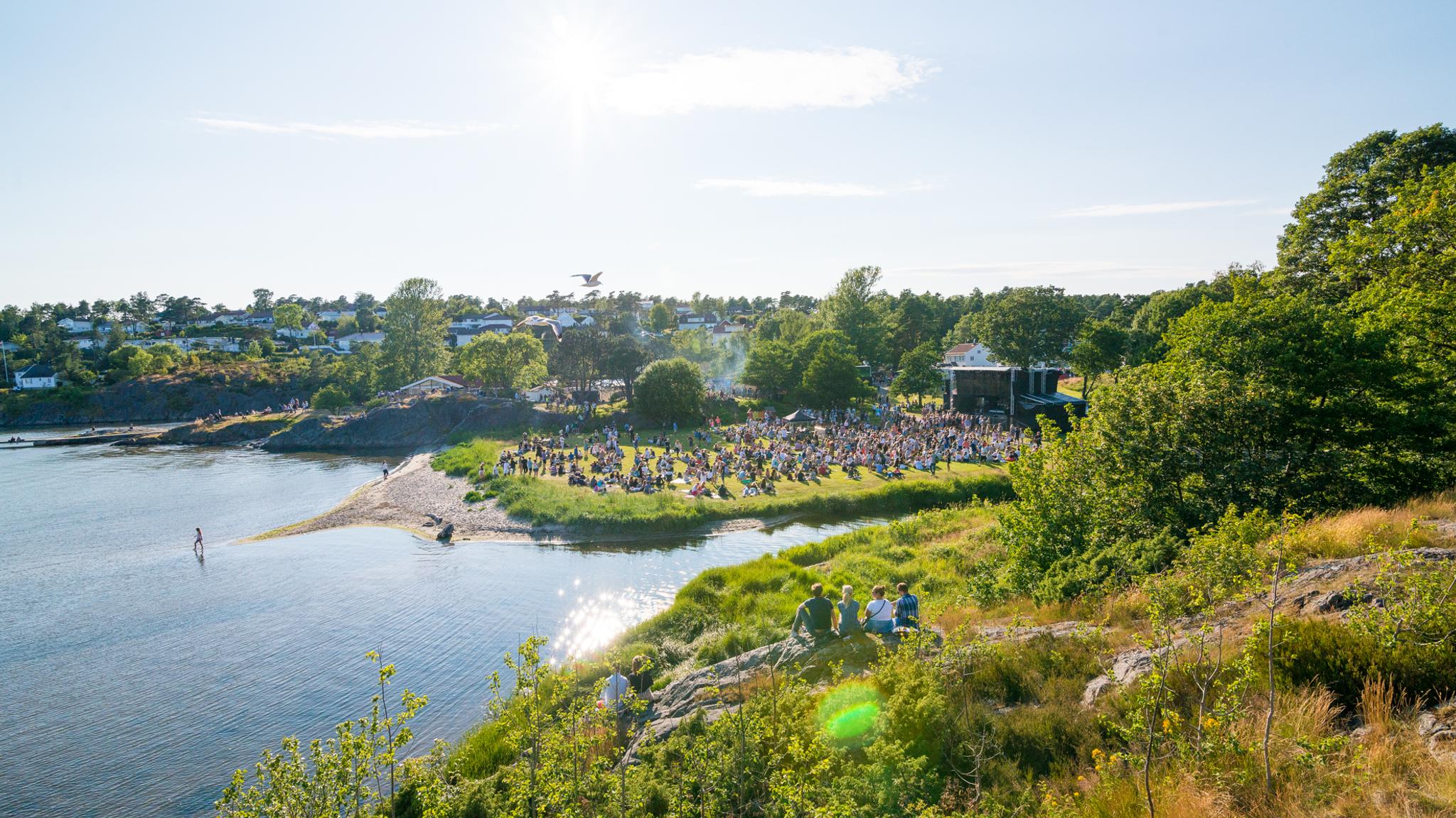 People sitting on the grass by the sea during Skral Festival in Grimstad in Southern Norway