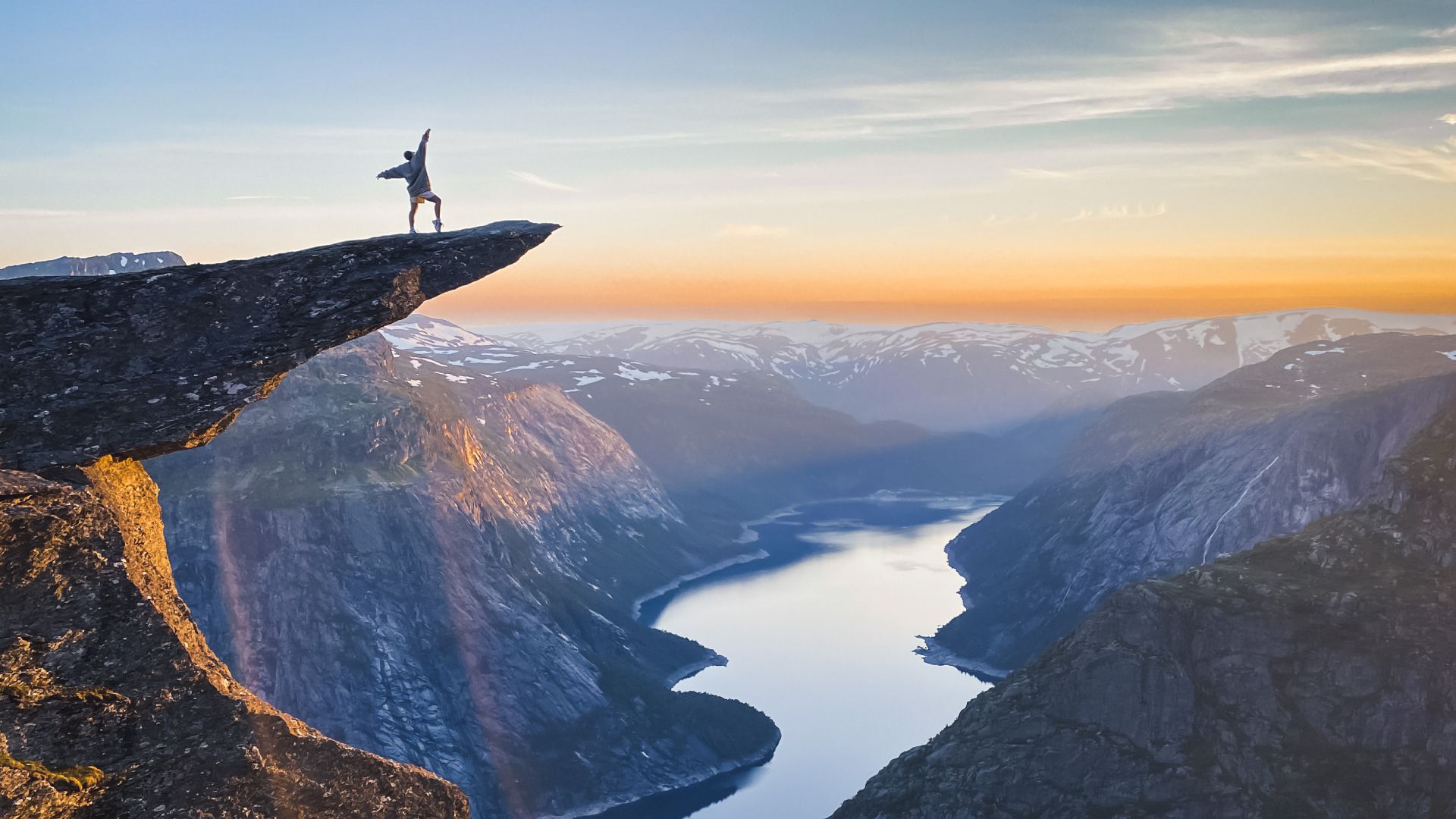 A person posing at the famous rock formation Trolltunga in sunset