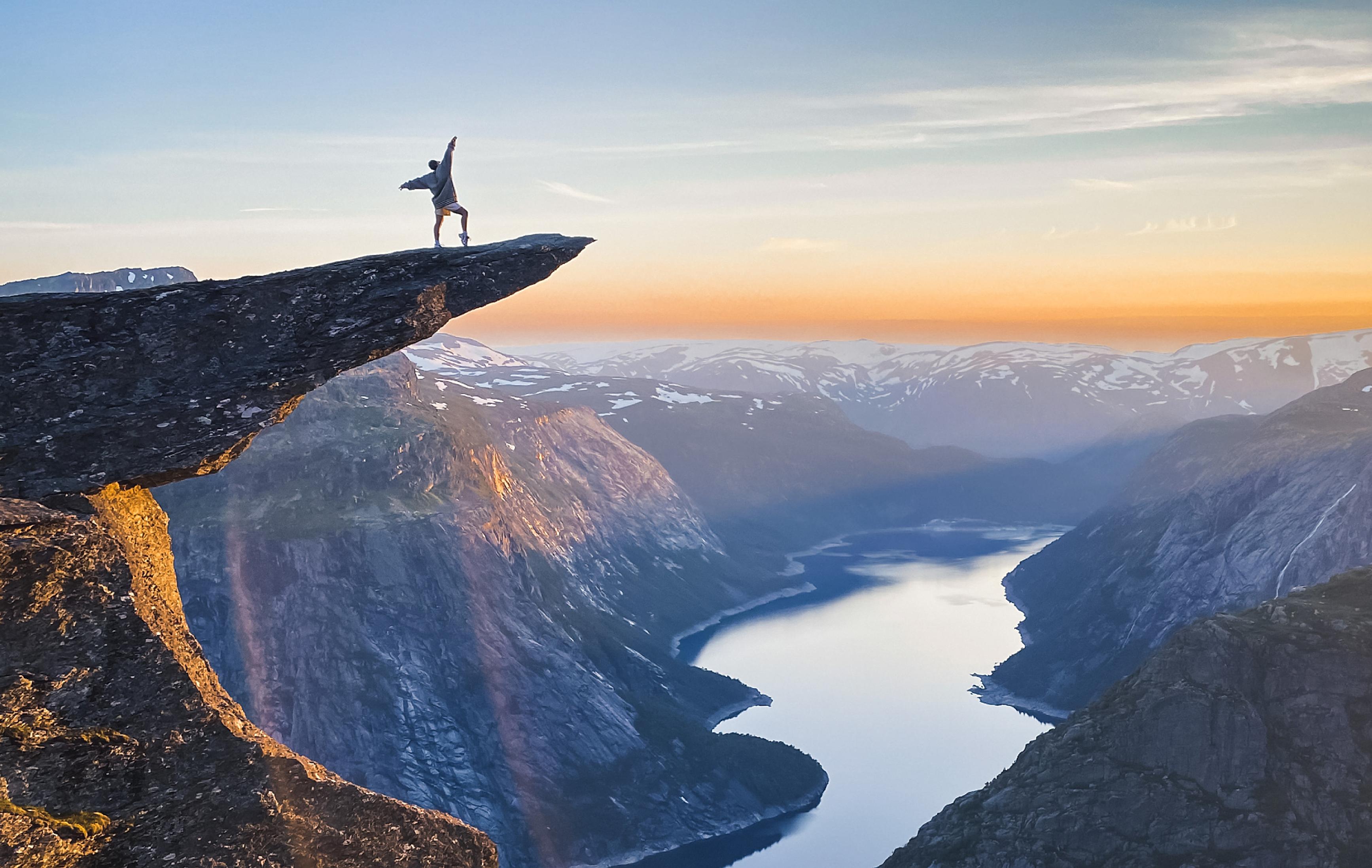 A person posing at the famous rock formation Trolltunga in sunset