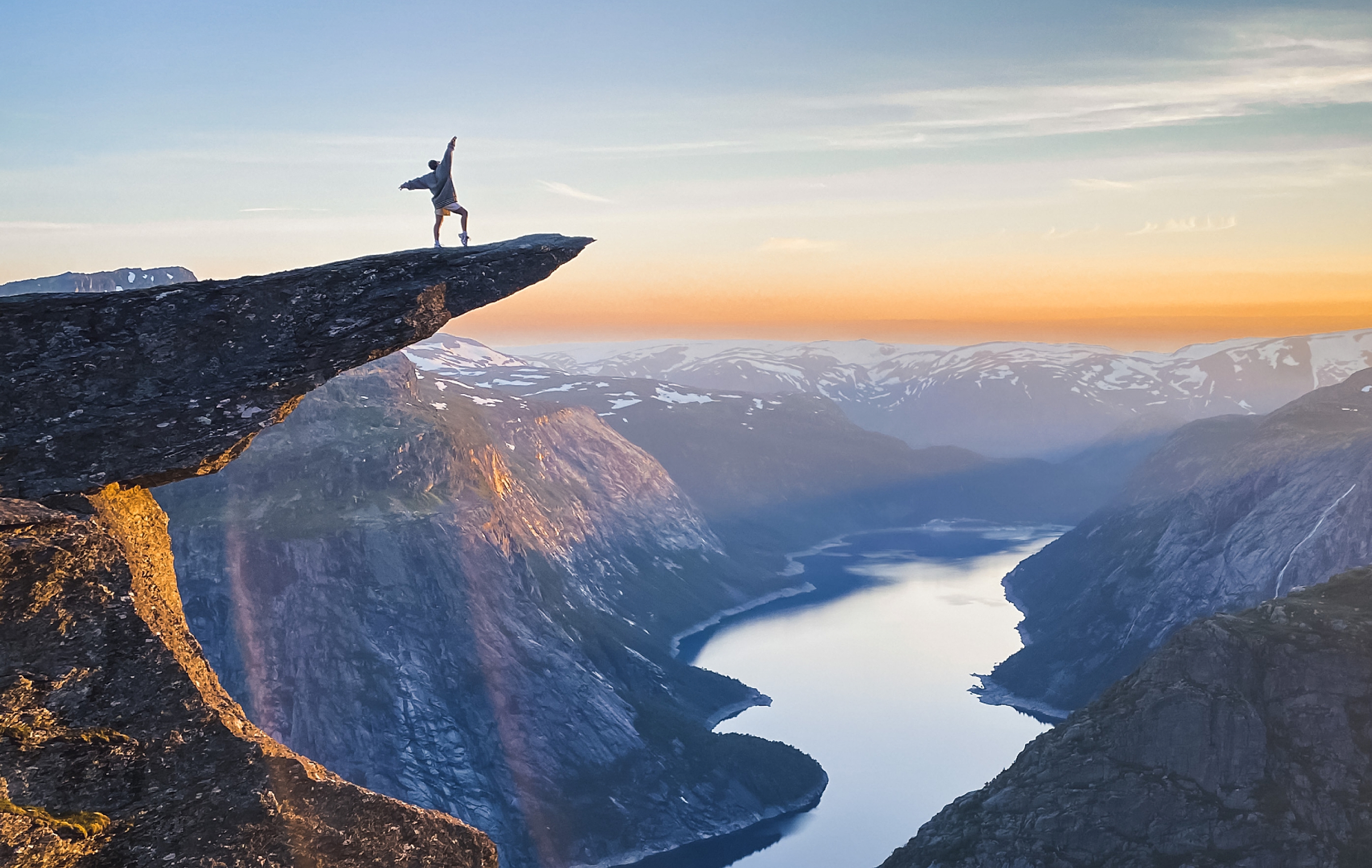 A person posing at the famous rock formation Trolltunga in sunset