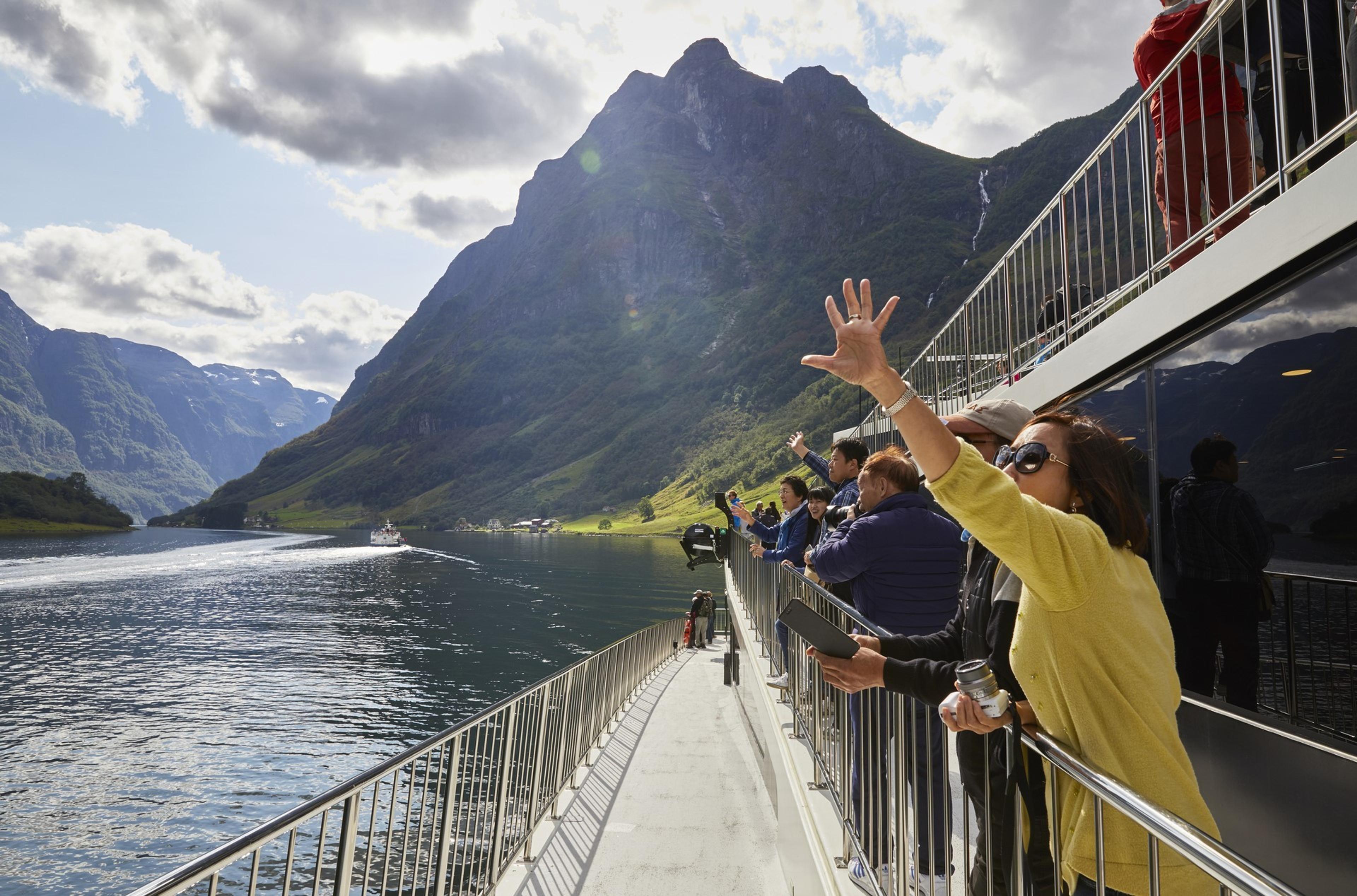 Tourists wave at passing boat while sailing througha norwegian fjord