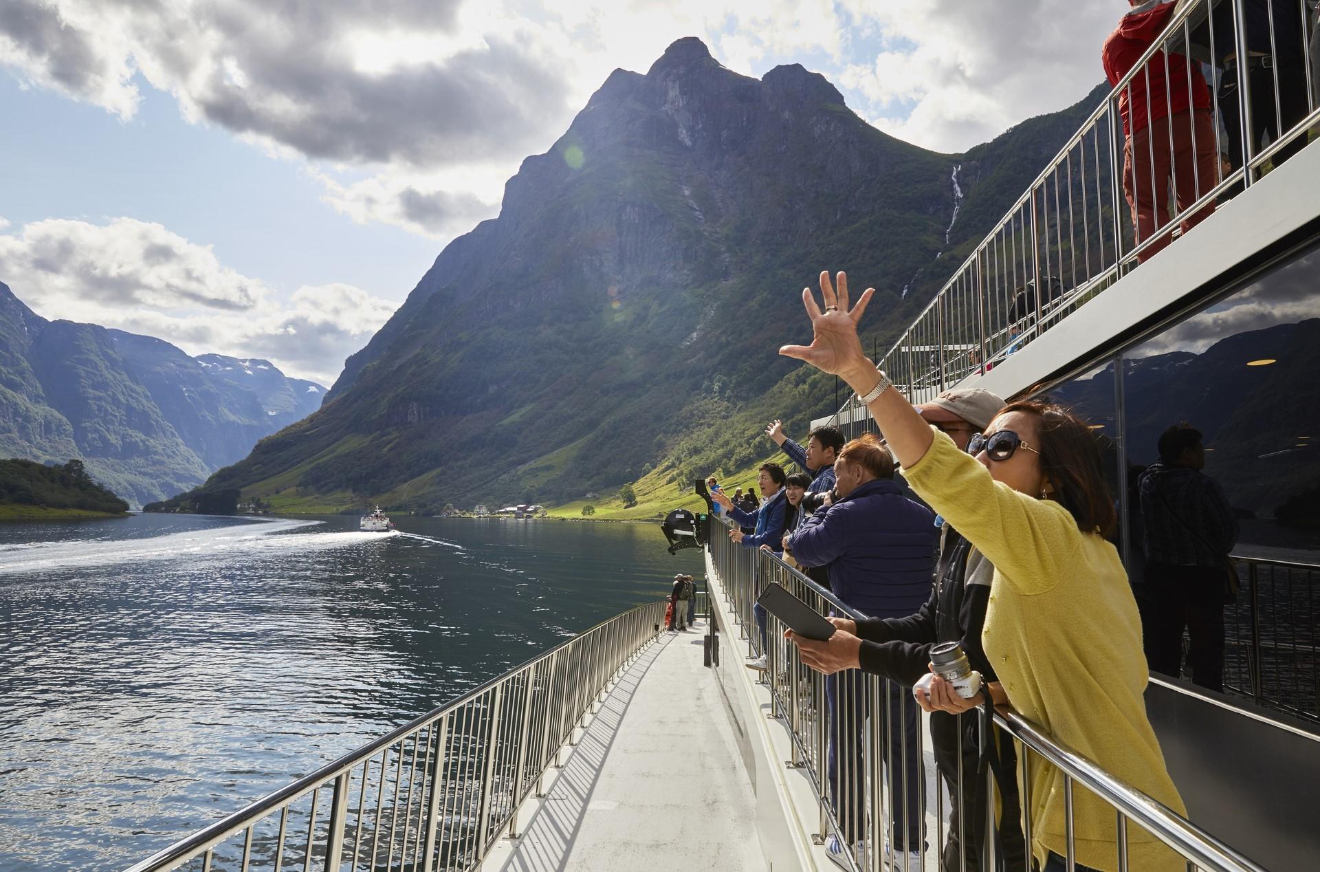 Tourists wave at passing boat while sailing througha norwegian fjord