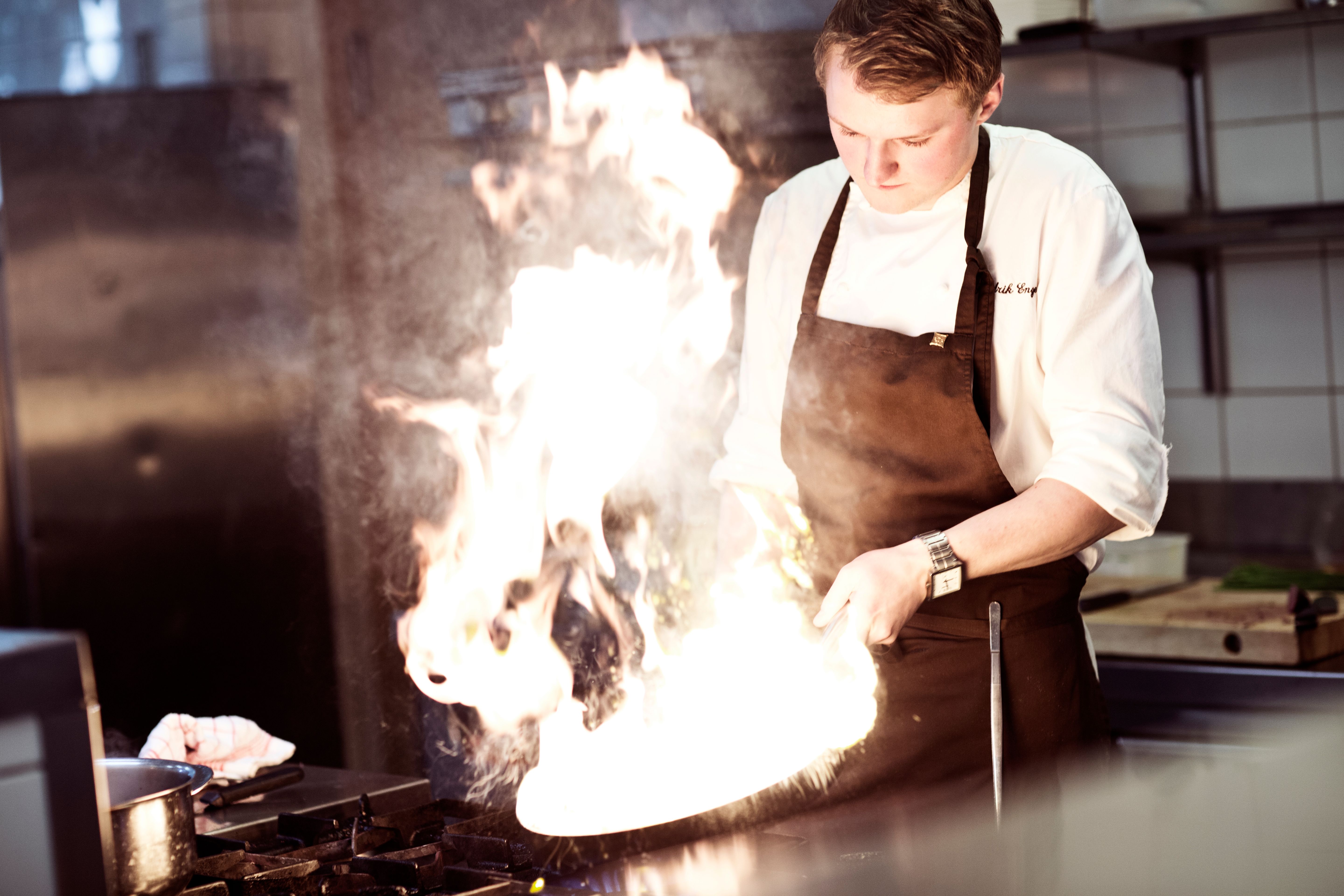 A chef cooking in a flaming pan in a kitchen