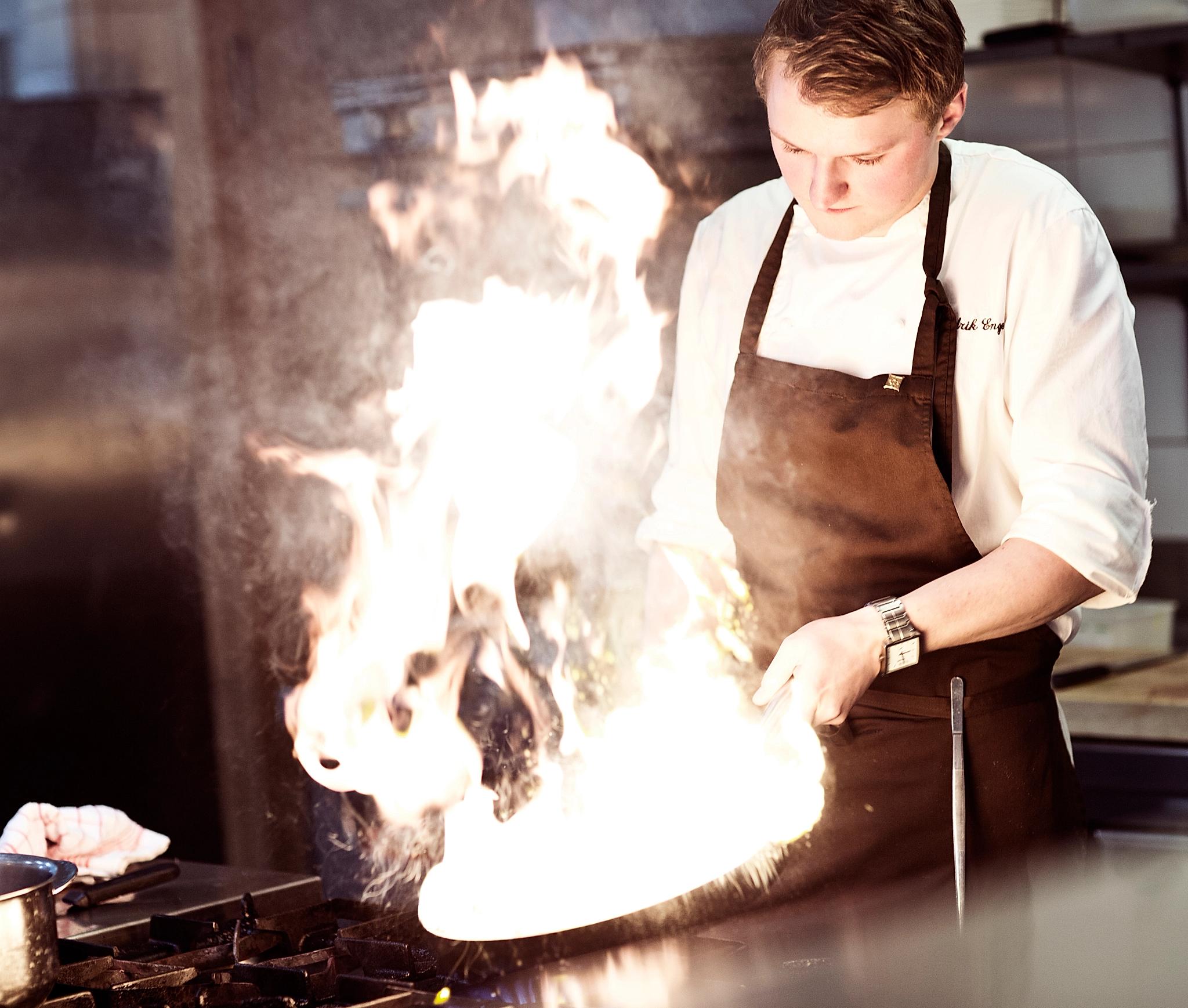 A chef cooking in a flaming pan in a kitchen