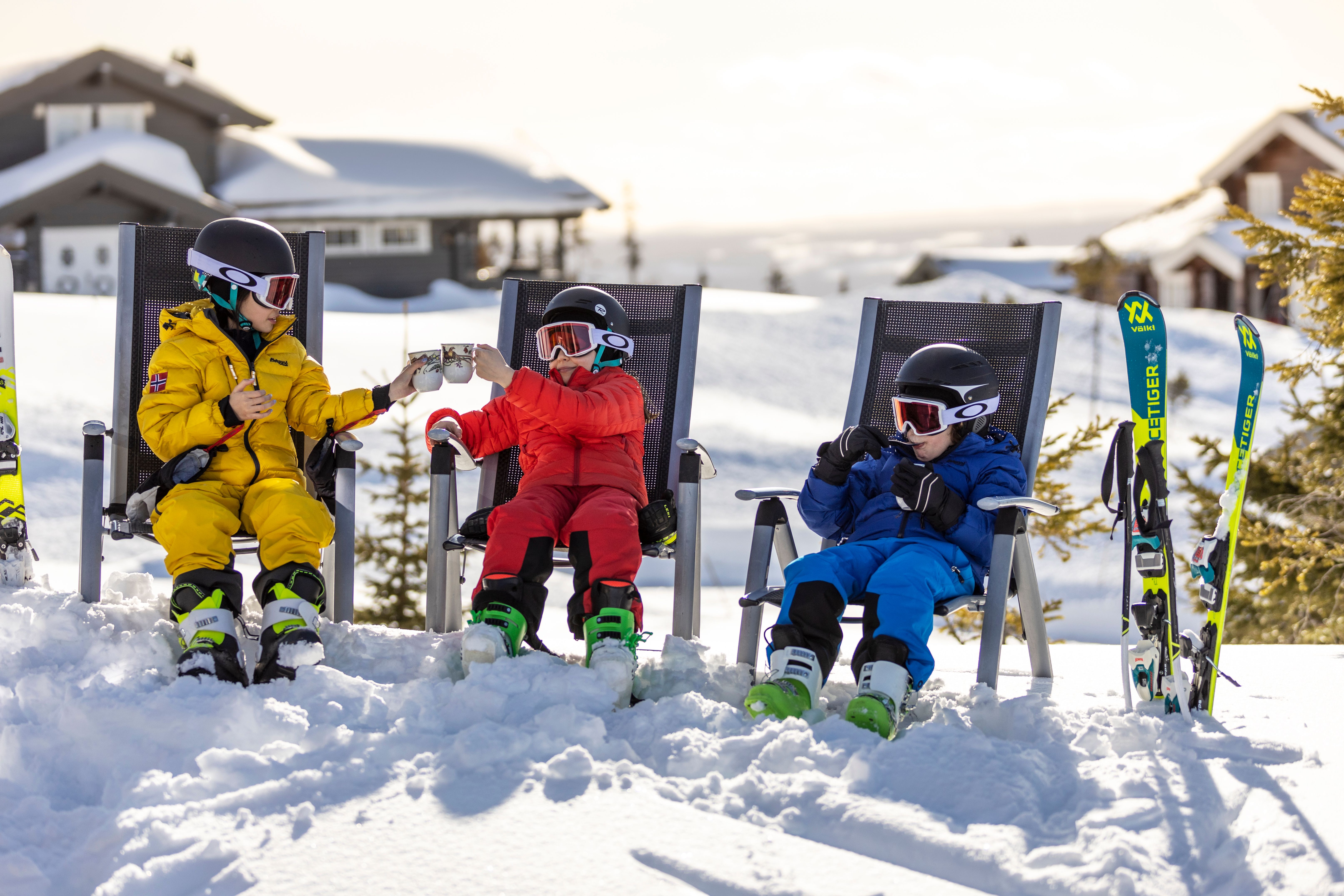 Three children enjoying snacks while taking a break from alpine skiing at one of the family-friendly ski resorts in Norway