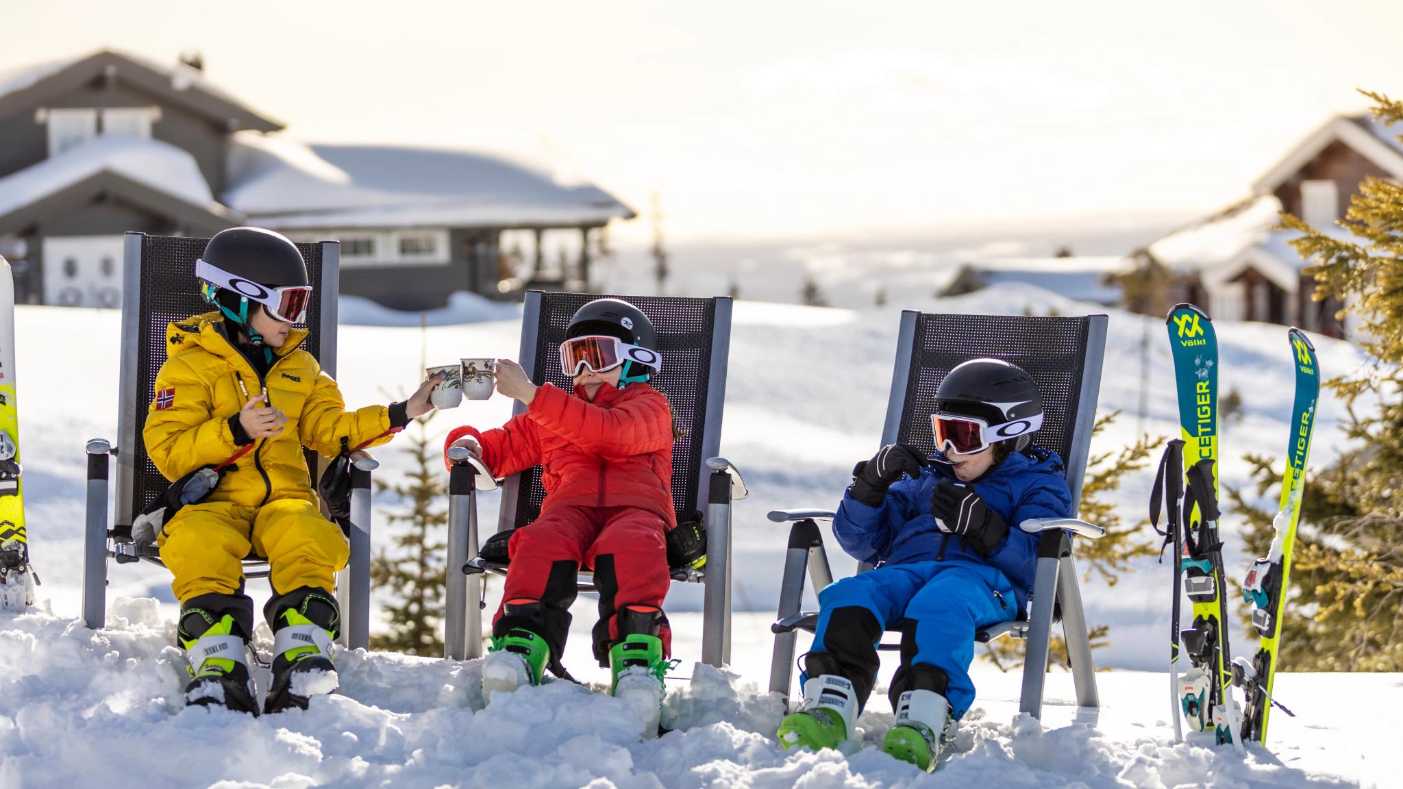 Three children enjoying snacks while taking a break from alpine skiing at one of the family-friendly ski resorts in Norway