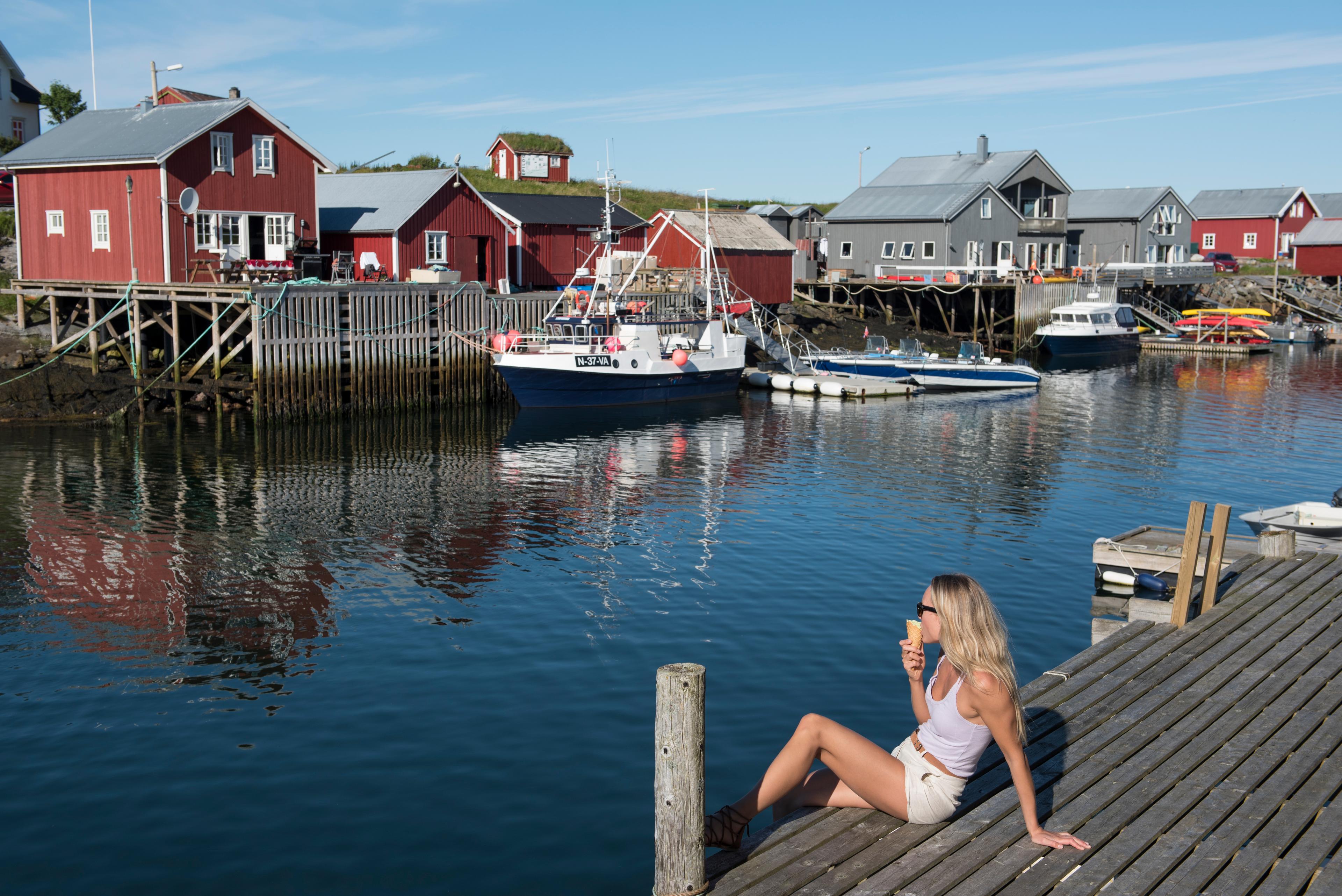 A woman sitting and eating an ice cream by the harbour on Vega in Helgeland, Northern Norway.