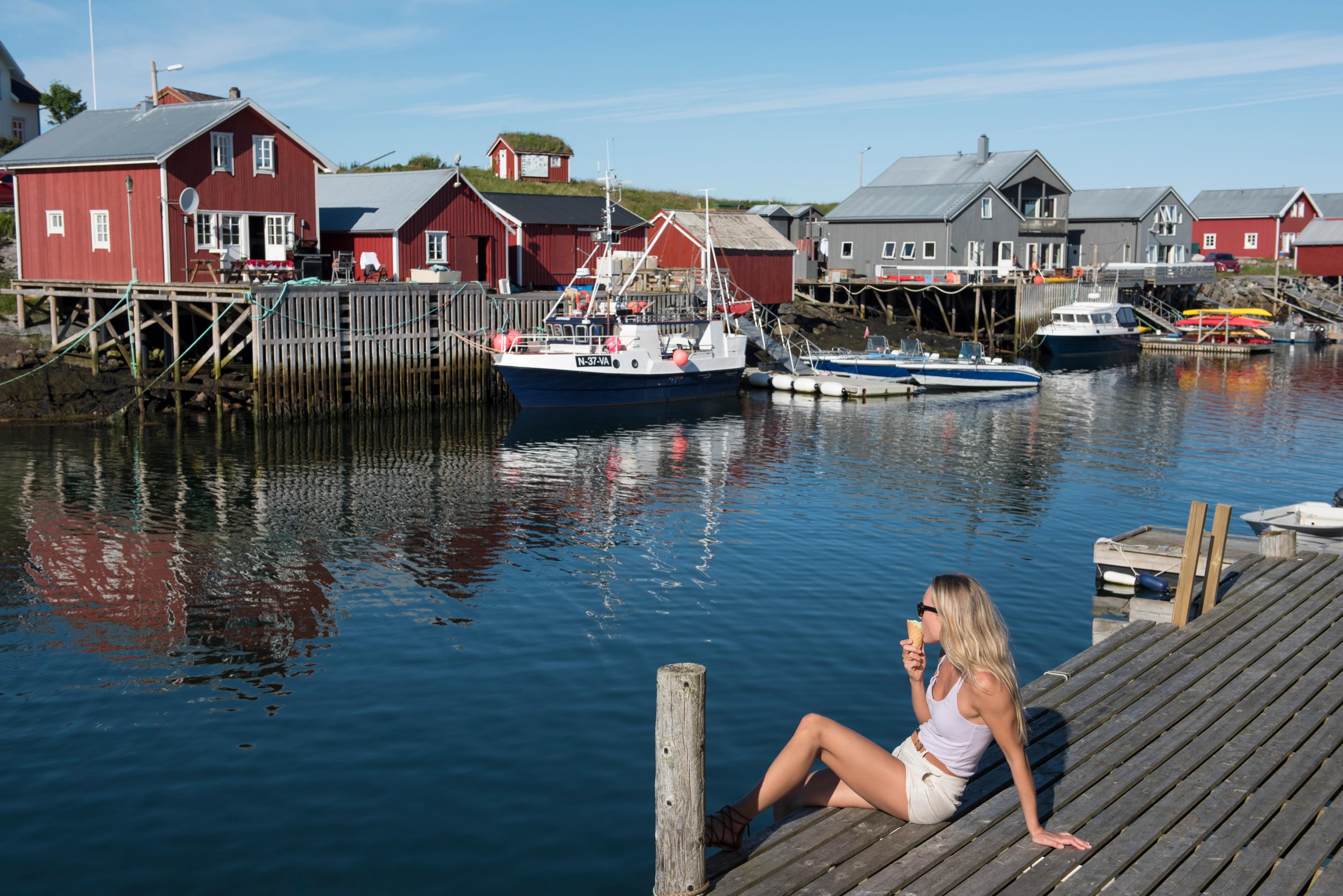 A woman sitting and eating an ice cream by the harbour on Vega in Helgeland, Northern Norway.