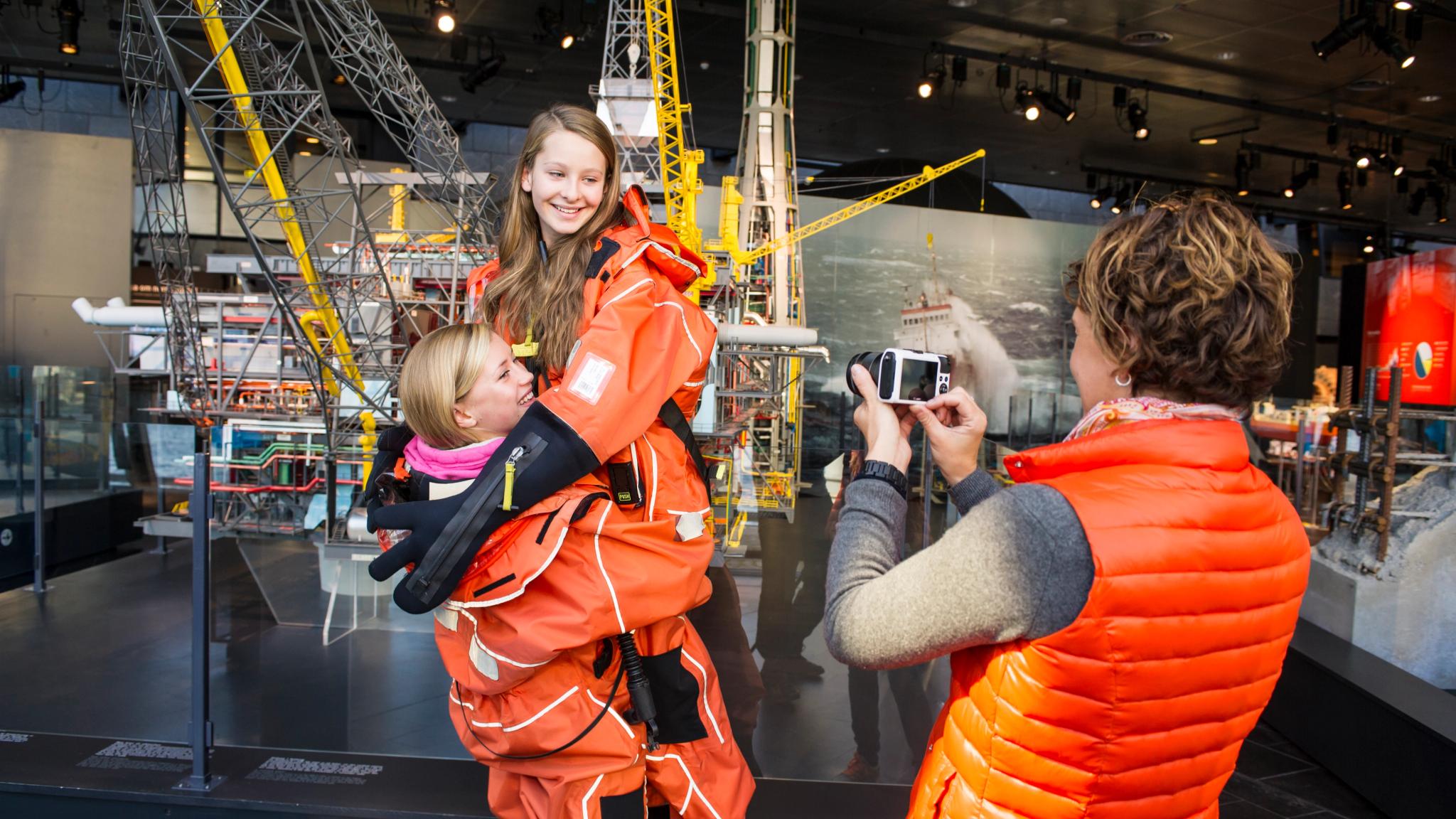 A woman taking picture of two girls in survival suits at Norwegian Petroleum Museum in Stavanger, Fjord Norway
