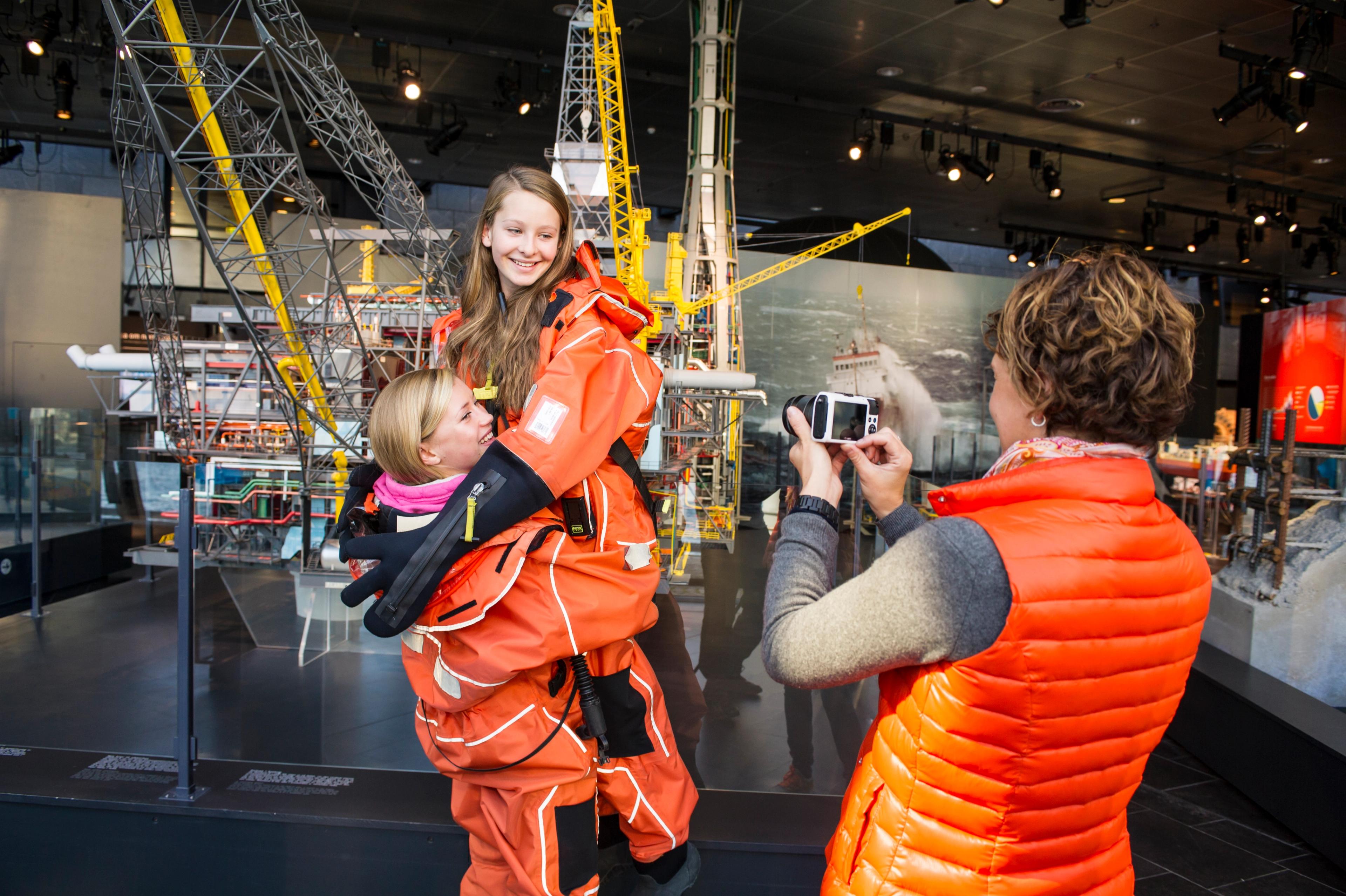 A woman taking picture of two girls in survival suits at Norwegian Petroleum Museum in Stavanger, Fjord Norway
