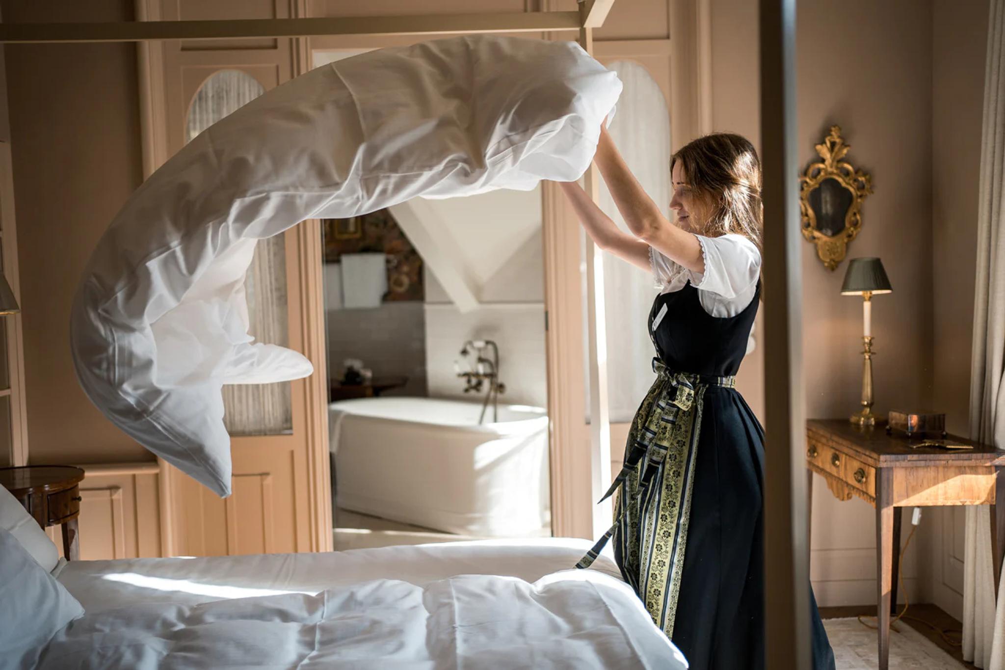 Staff member making bed in elegant historic hotel room.